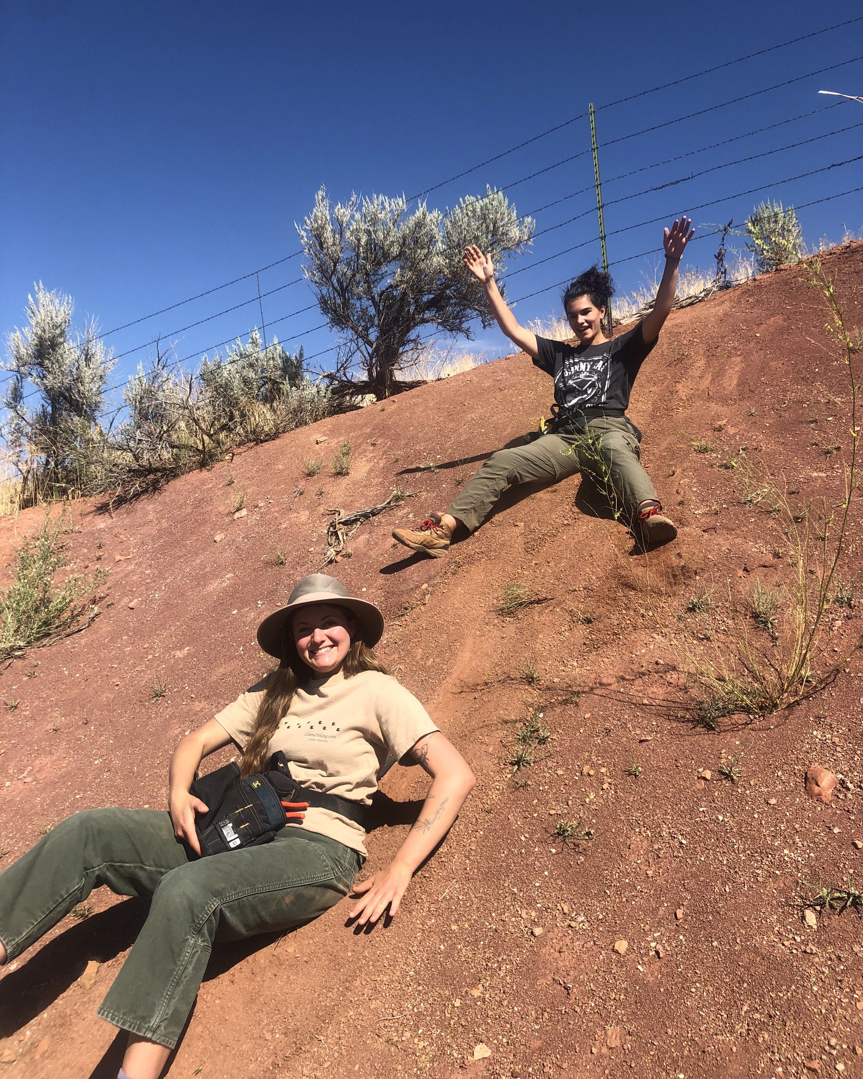 Photo of GeoCorps Participant in the field sliding down red clay slope