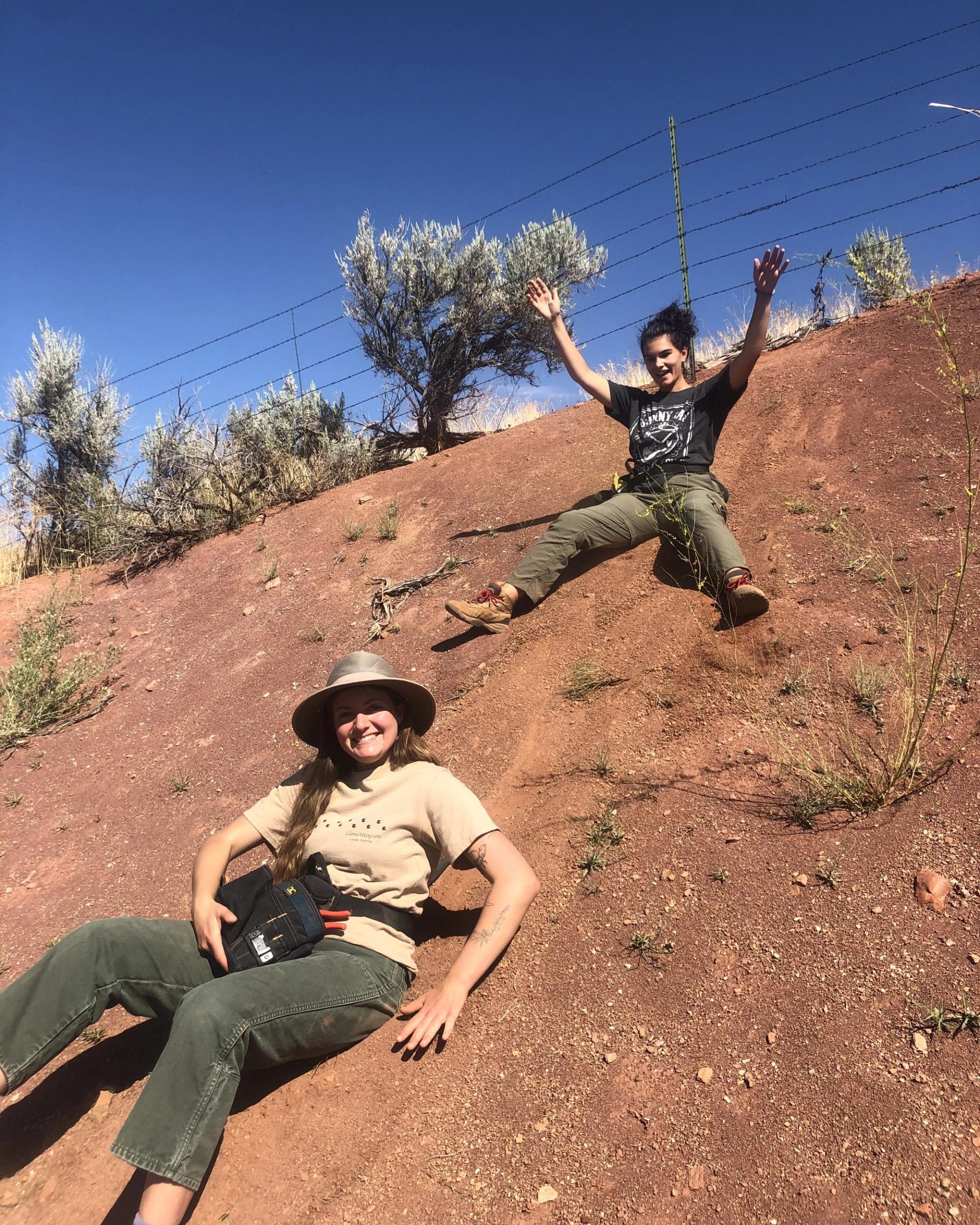 Photo of GeoCorps Participant in the field sliding down red clay slope