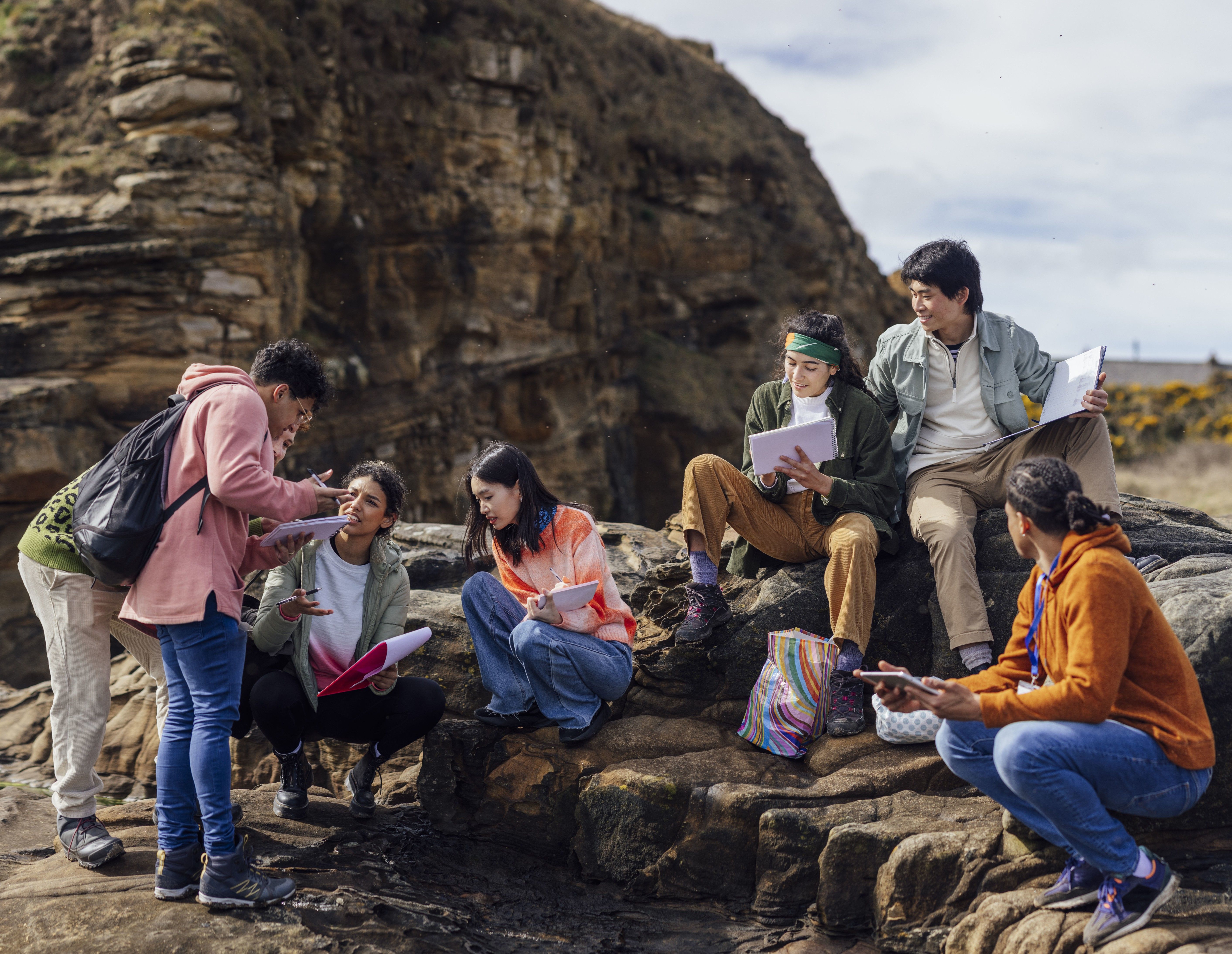 GSA partners on rocky terrain near cliffs, engaged in conversation and holding notebooks. They appear relaxed and immersed in nature.