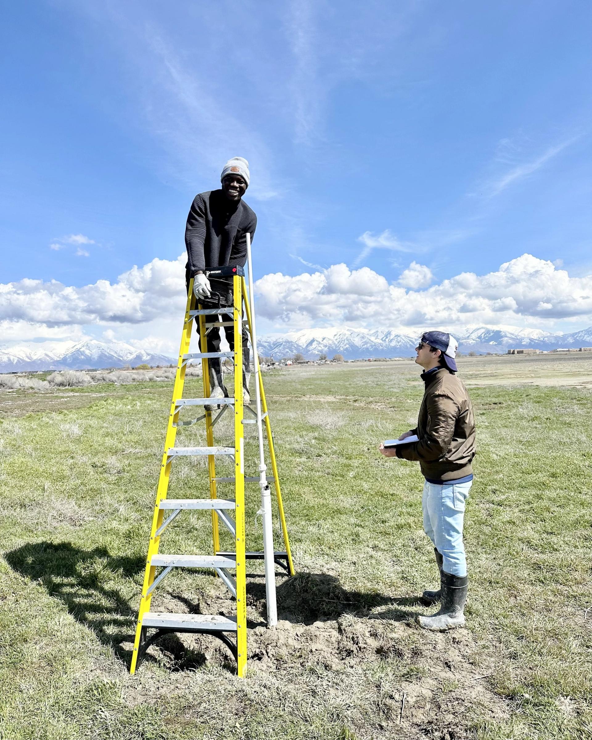 Photo of GSA graduate student research grant recipients conducting geoscience research in the field on a ladder with mountains in the background