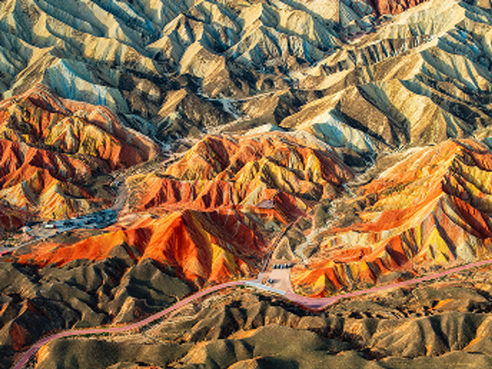 Aerial view of vibrant, multicolored Zhangye Danxia landforms in China. Undulating layers of red, yellow, and orange create a surreal, striking landscape.