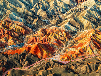 Aerial view of vibrant, multicolored Zhangye Danxia landforms in China. Undulating layers of red, yellow, and orange create a surreal, striking landscape.