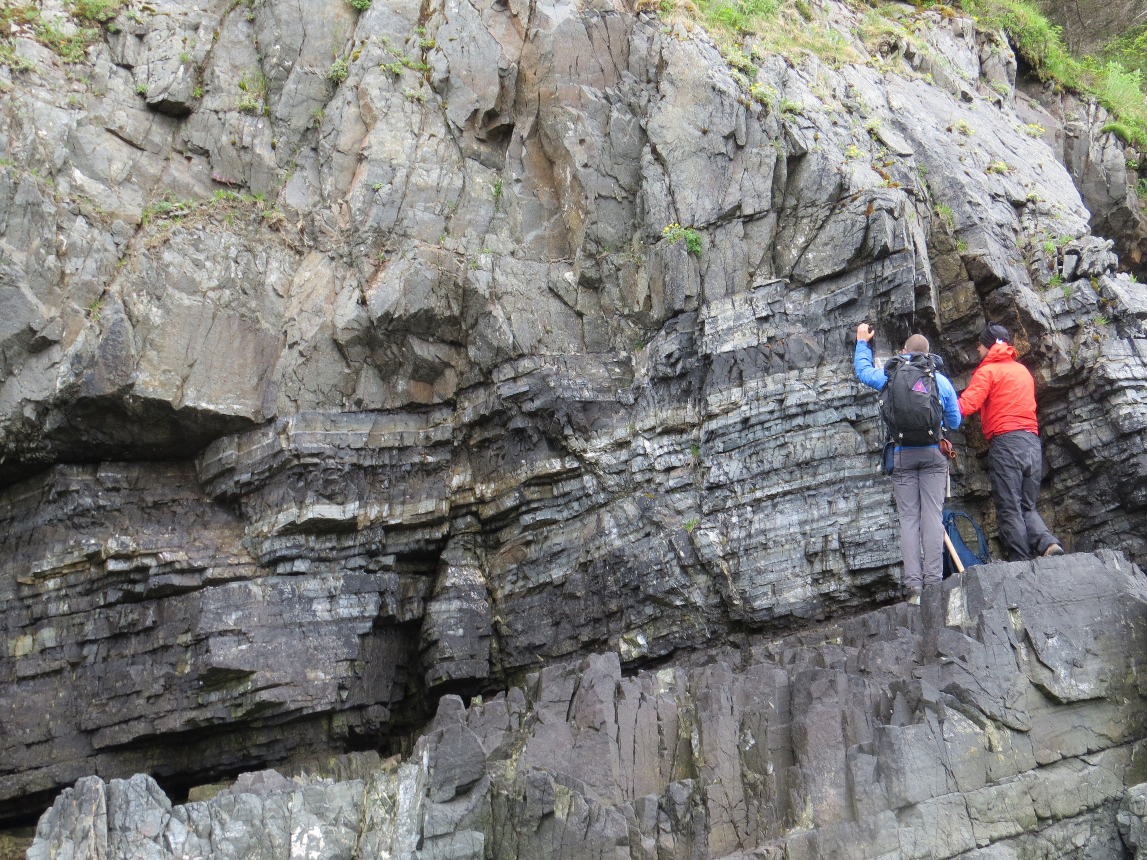 Photo of GSA Graduate Student Research Grant Recipients conducting geoscience research fieldwork on large rock outcrop with angled layers of rock