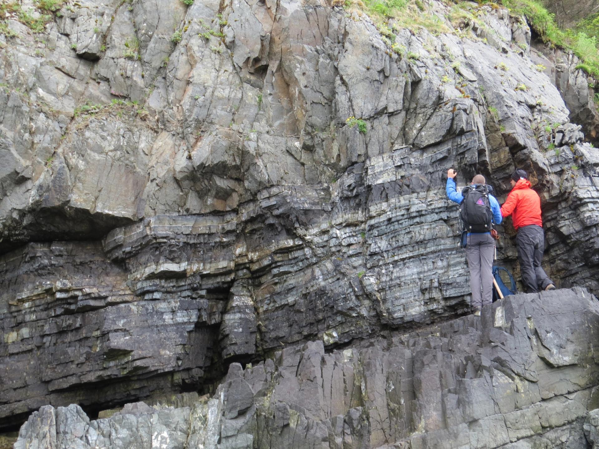 Photo of GSA Graduate Student Research Grant Recipients conducting geoscience research fieldwork on large rock outcrop with angled layers of rock