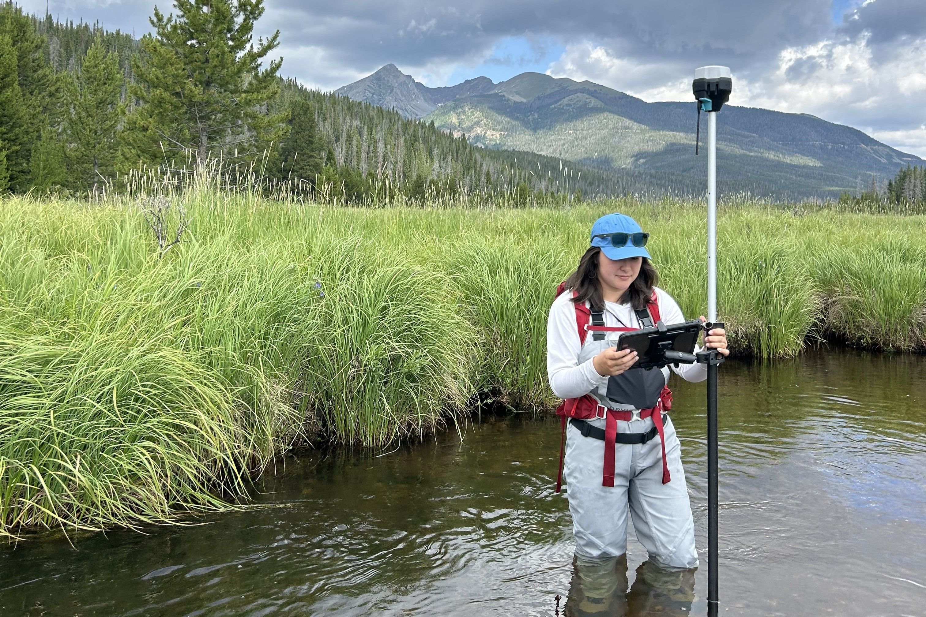 Graduate Student Research Grant recipient taking stream measurements in the field with beautiful mountains in the background