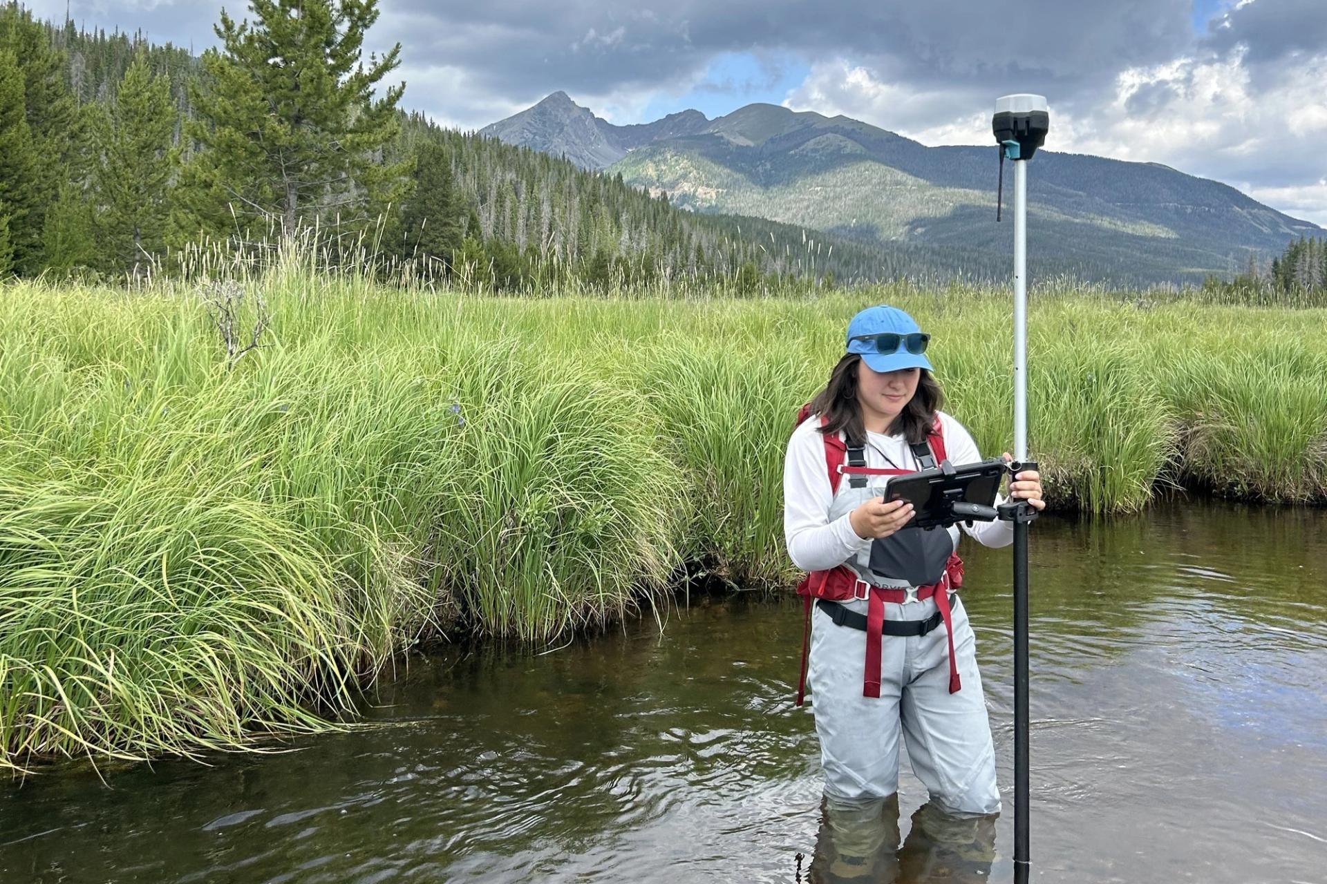 Graduate Student Research Grant recipient taking stream measurements in the field with beautiful mountains in the background