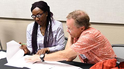 Two people sit at a table, reviewing papers.