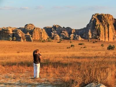Woman standing in field with mountains in the distance taking a photo.