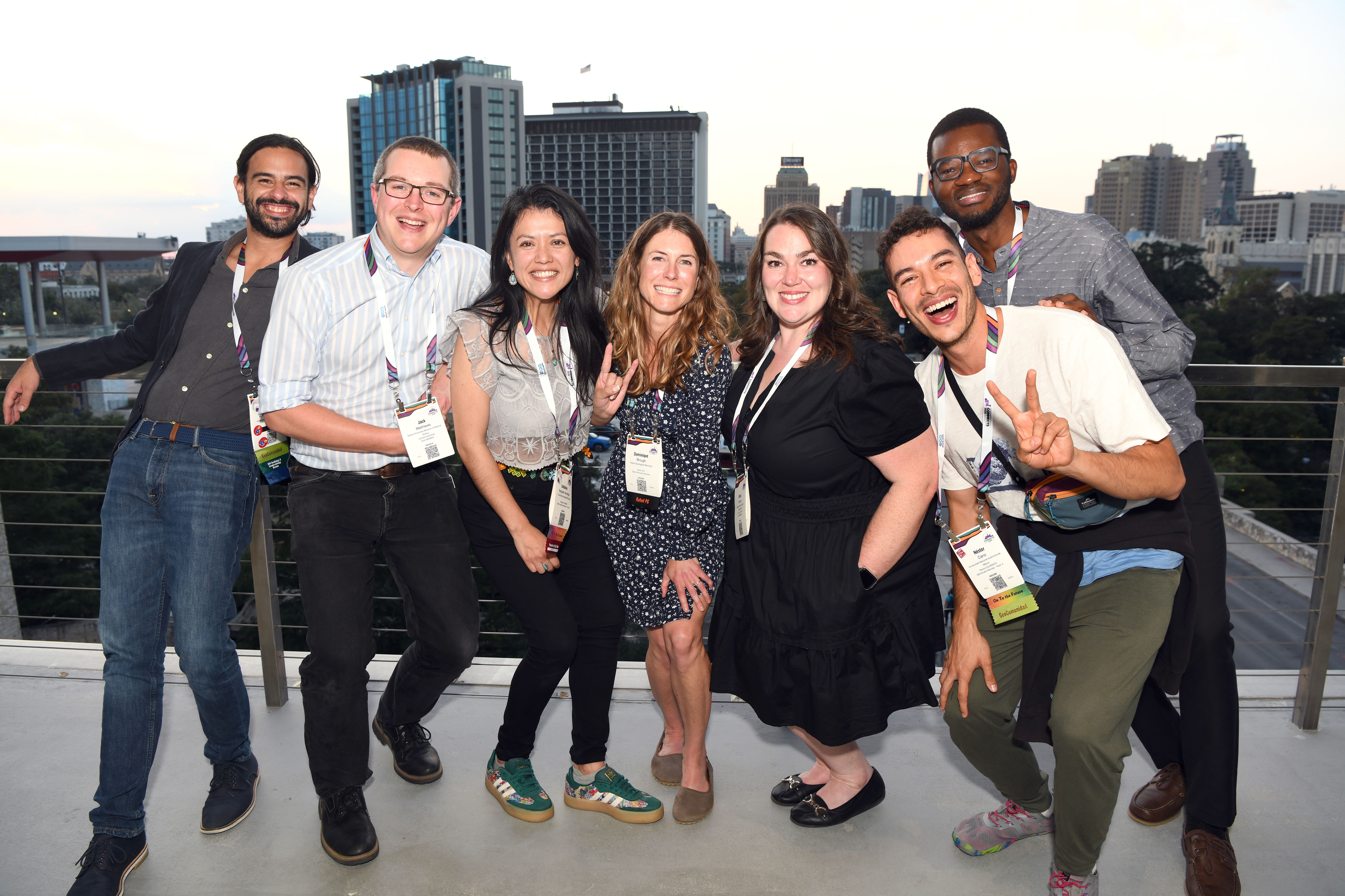 A group of seven GSA Connects 2025 attendees smile and pose together on a rooftop terrace, with a San Antonio skyline visible in the background at dusk.