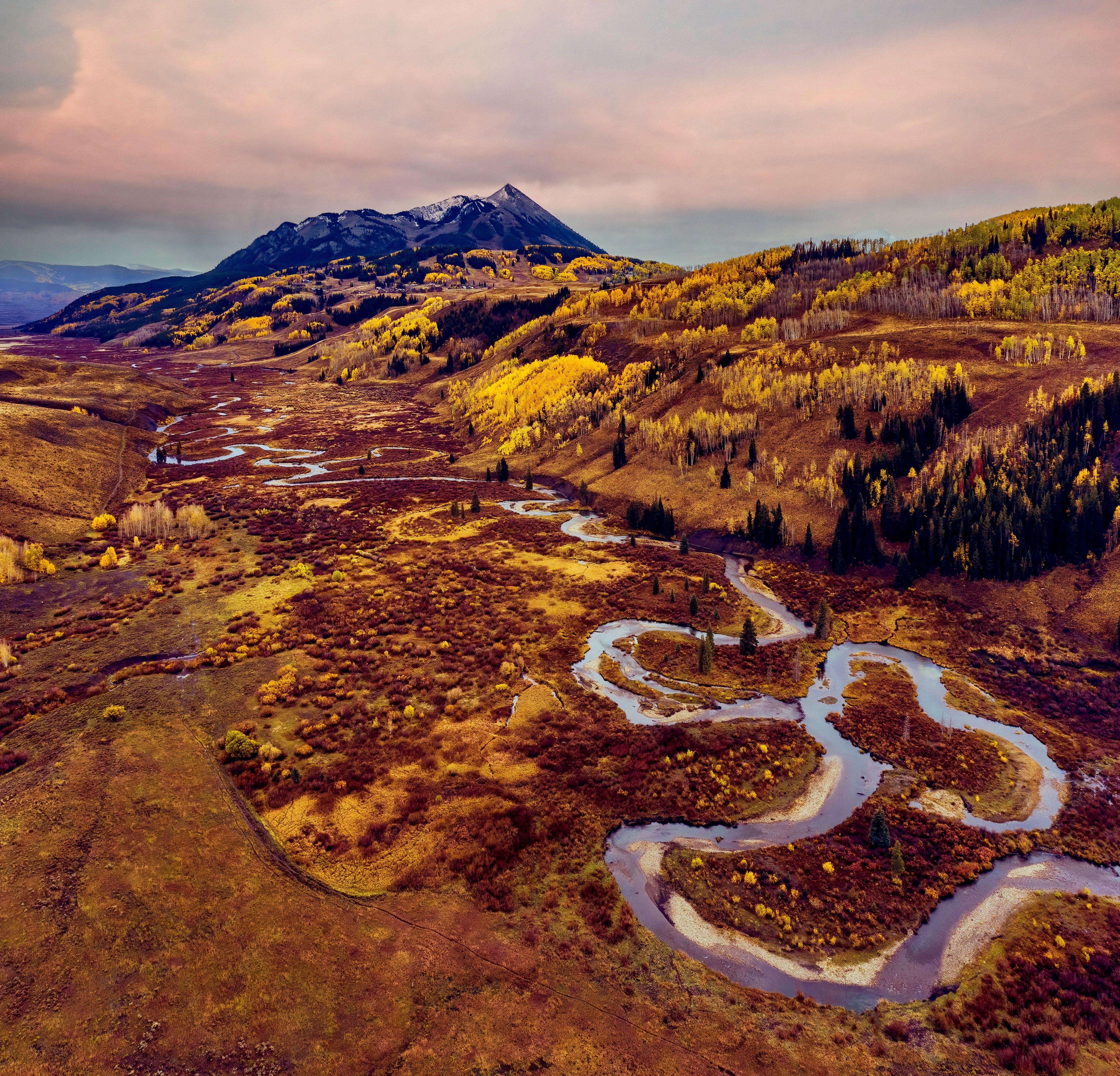 View of Crested Butte Mountain with the meandering East River in the foreground taken from a drone with golden aspen trees
