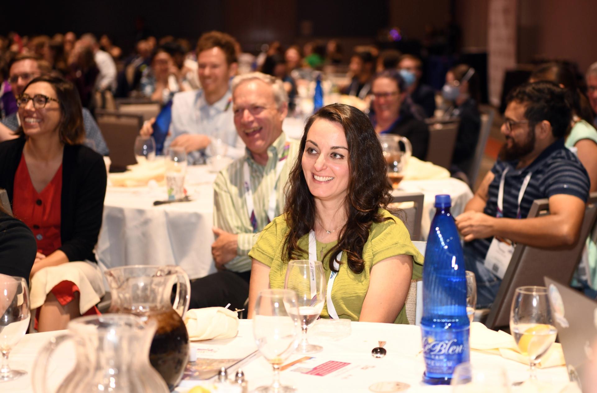 A crowd listens and takes notes in a conference setting.