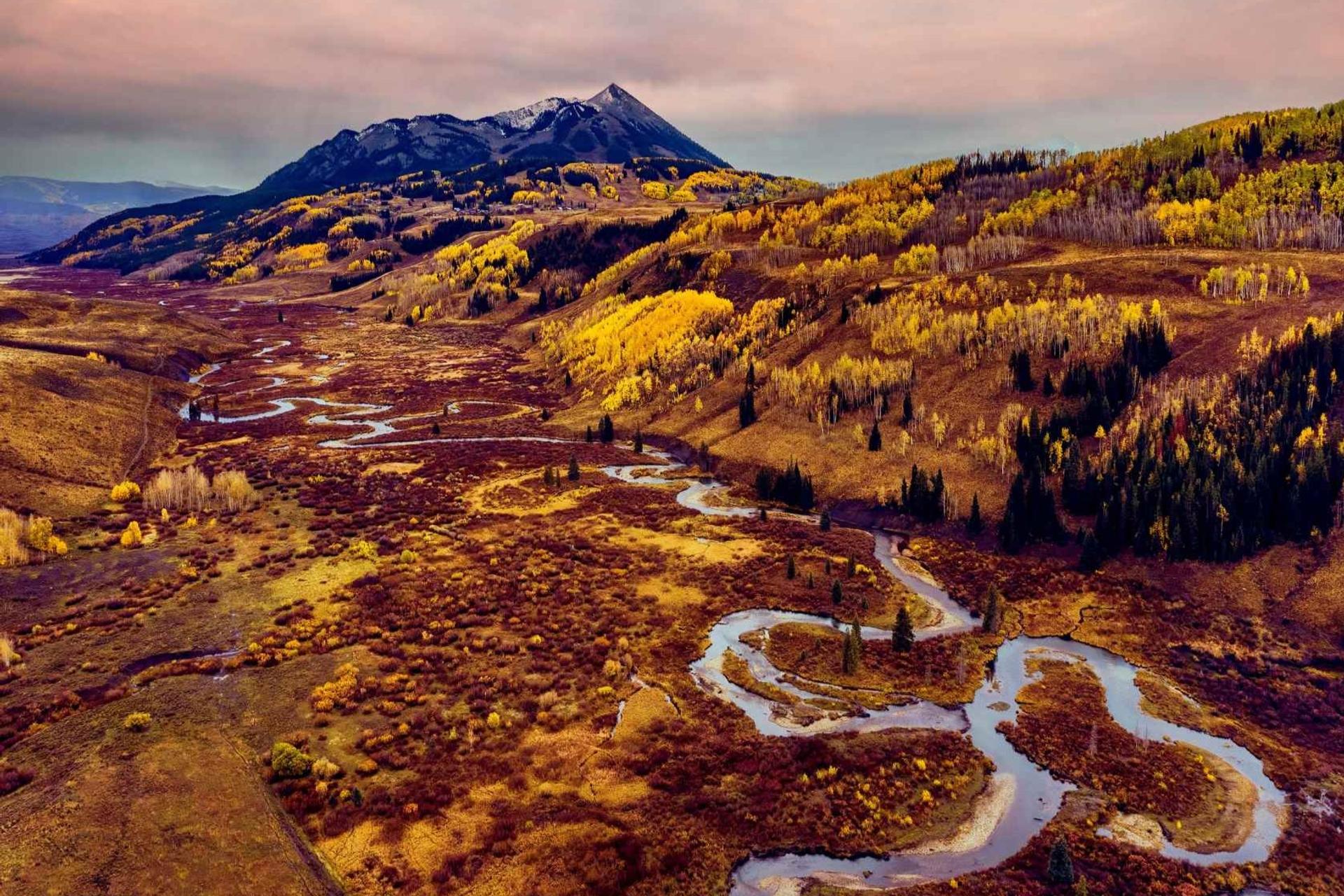 View of Crested Butte Mountain with the meandering East River in the foreground taken from a drone with golden aspen trees