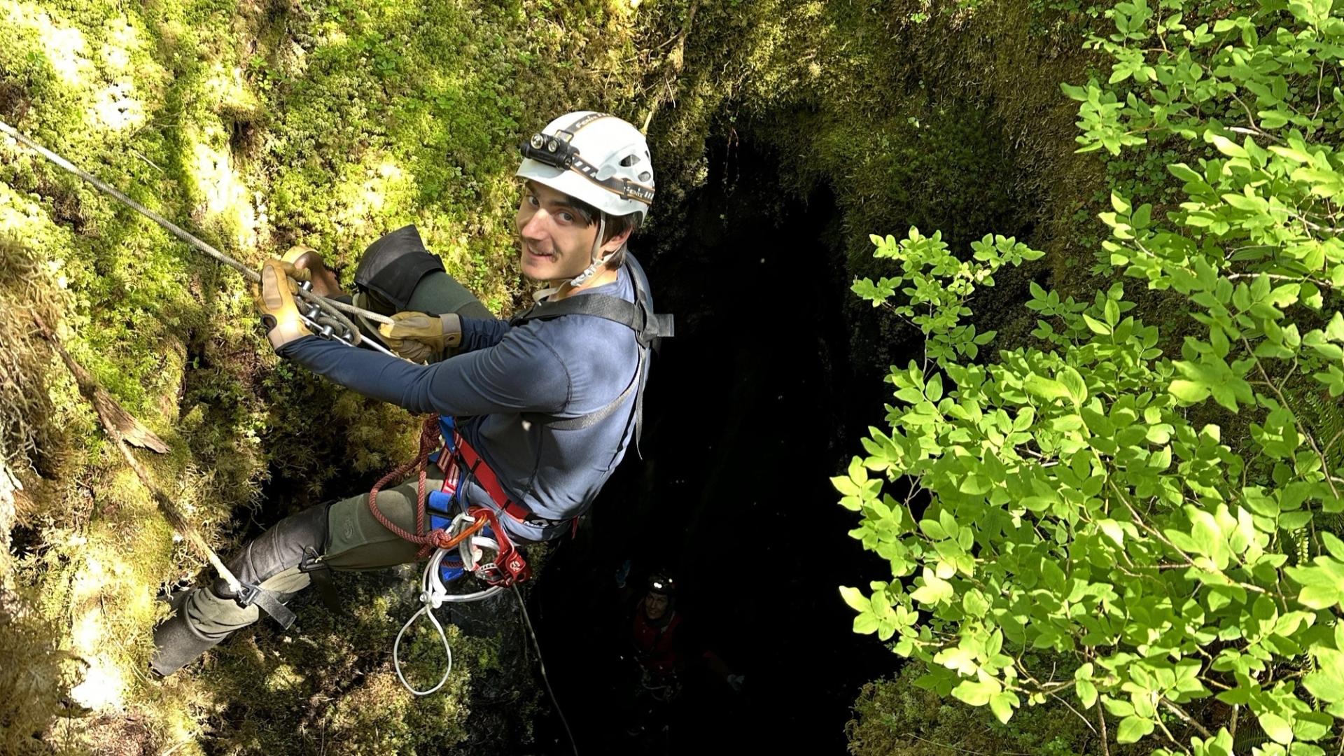 Student climbing down a hole in field with hard hat on