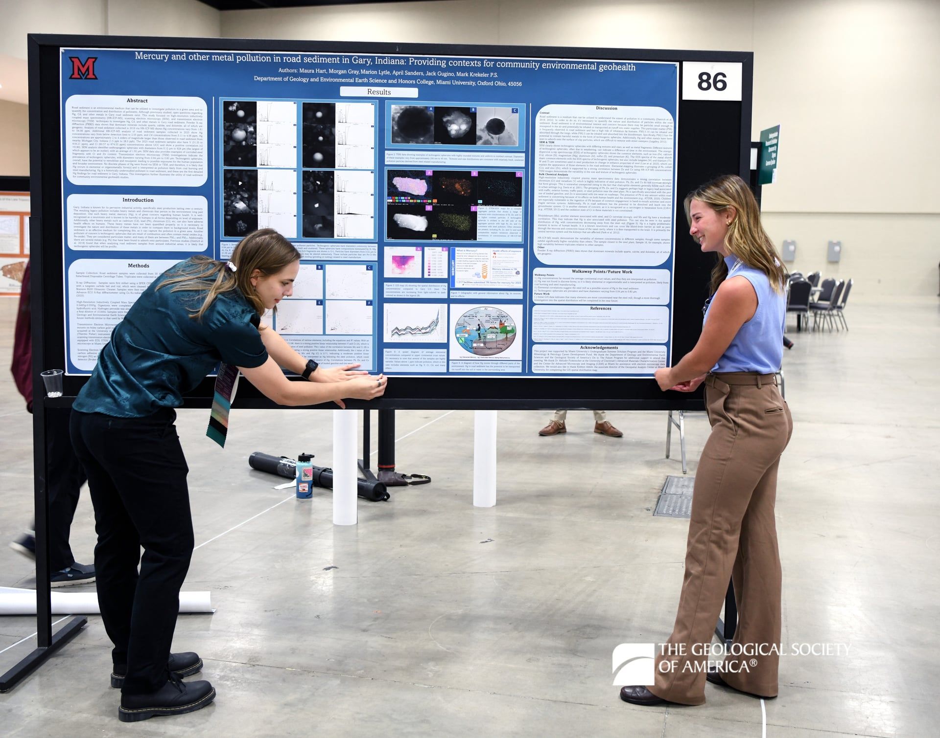 Two GSA Connects 2025 attendees stand and pin a large, printed poster to a black poster stand.