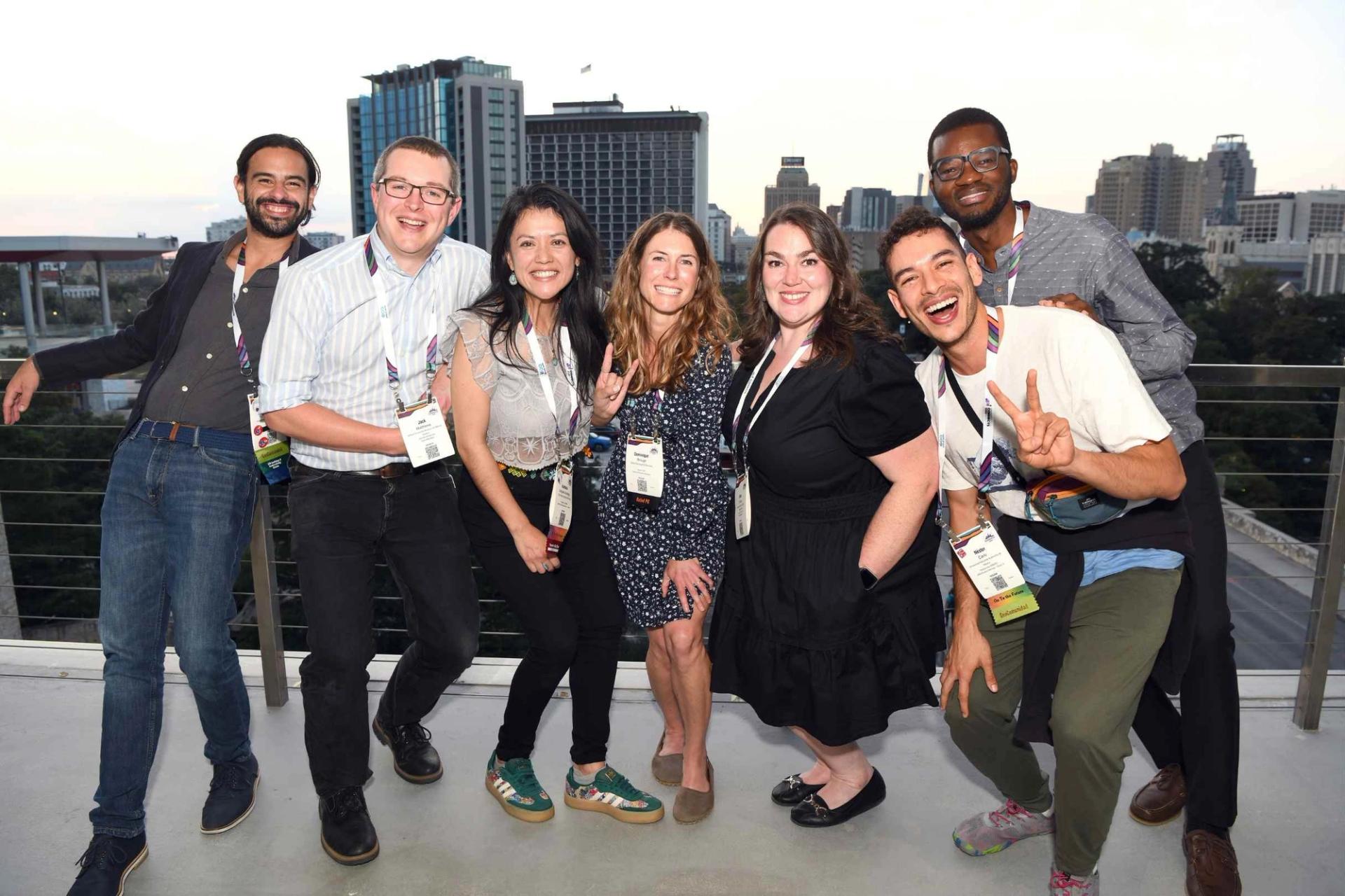 A group of seven GSA Connects 2025 attendees smile and pose together on a rooftop terrace, with a San Antonio skyline visible in the background at dusk.