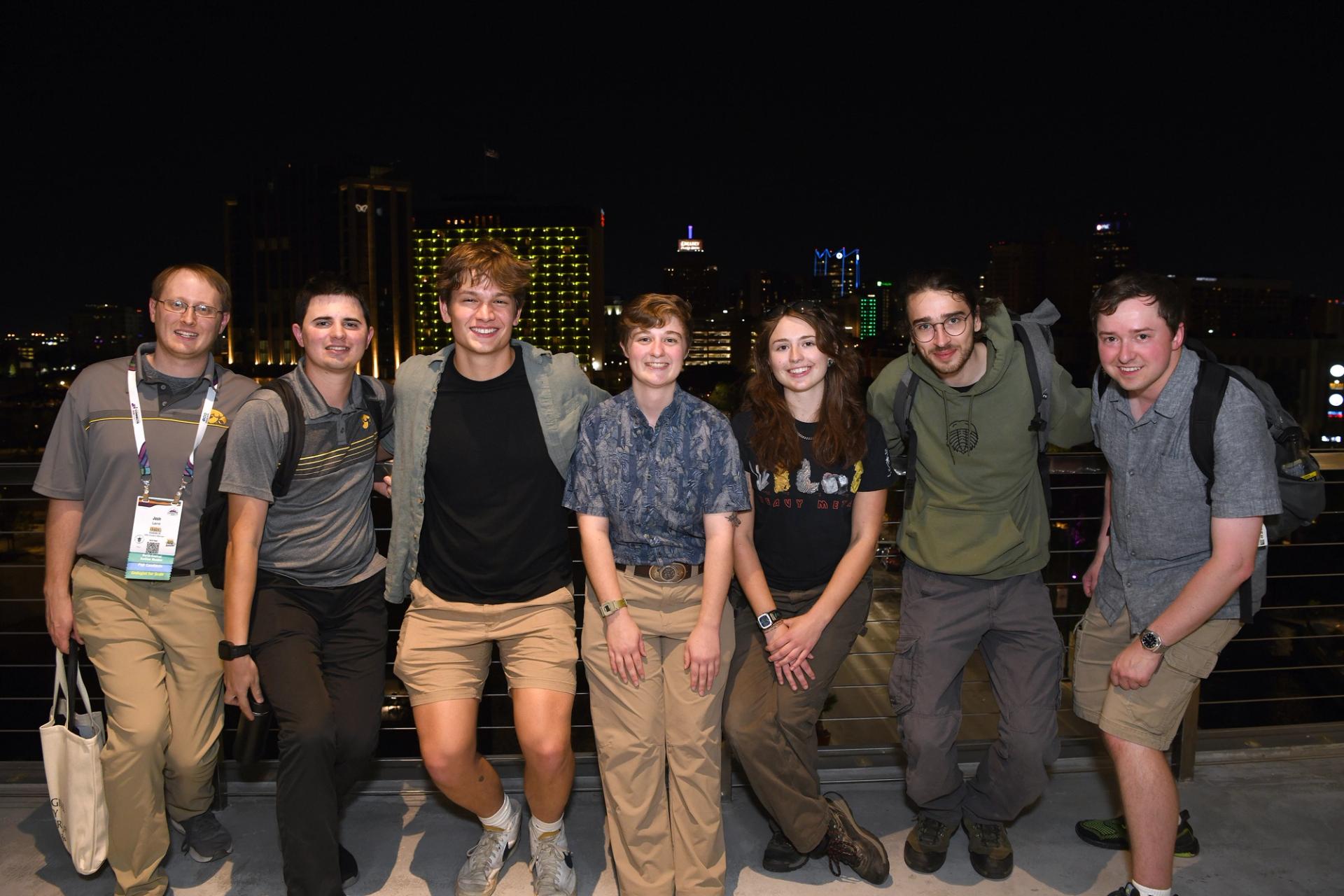 A group of seven smiling GSA Connects 2025 attendees pose together on an outdoor rooftop terrace at night, with a glowing San Antonio skyline visible behind them.