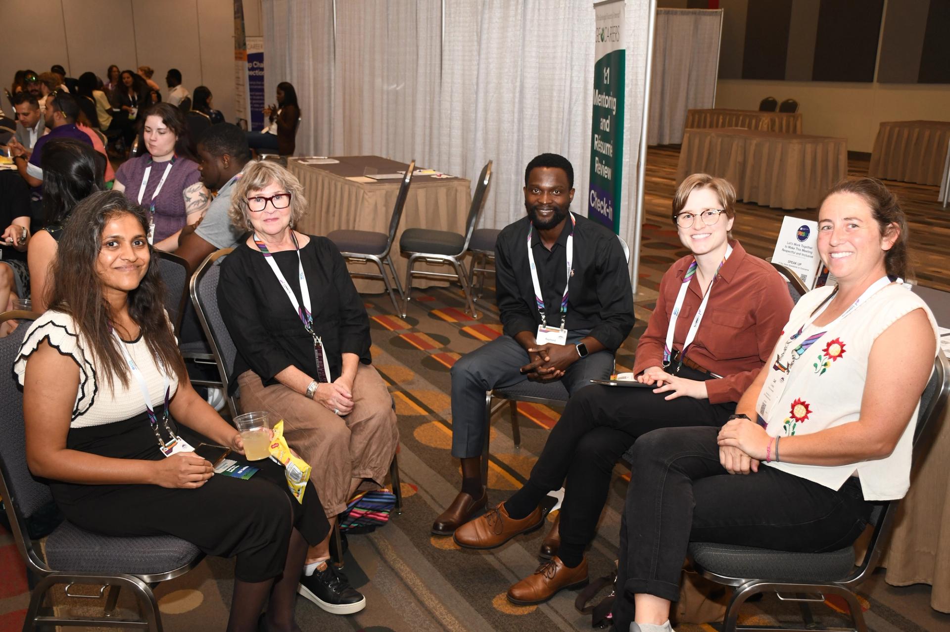 Three smiling female GSA conference attendees of different generations pose together in a large conference ballroom, with one wearing a GSA Fellow badge ribbon and a RISE button, and a projected presentation screen visible in the background.