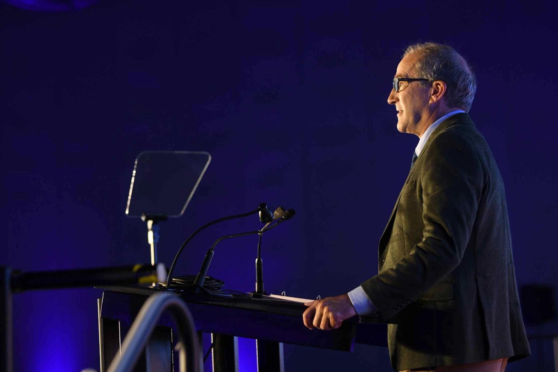 A man presents at a podium in front of a crowd.
