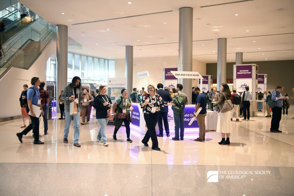 A smiling GSA Connects 2025 attendee leads a group of 3 people past the Registration area.