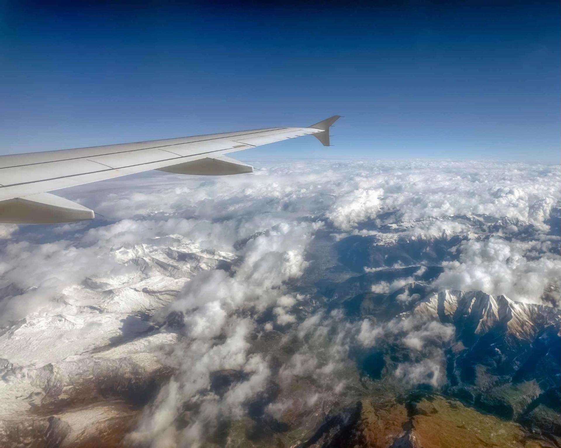 Aerial view of the Central Alps with snow capped mountains and airplane wing under bright blue sky