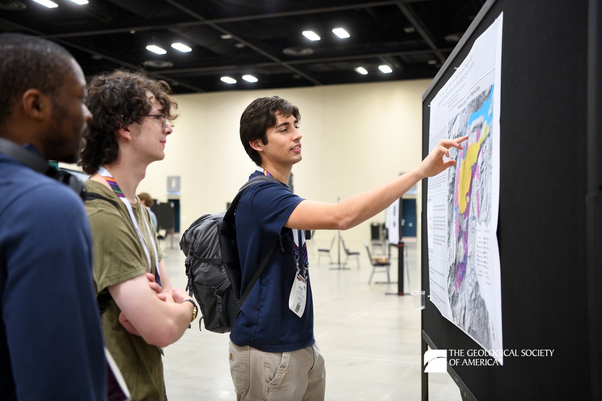 A GSA Connects 2025 poster presenter points to a section on their poster for two attendees who have stopped to examine the poster.