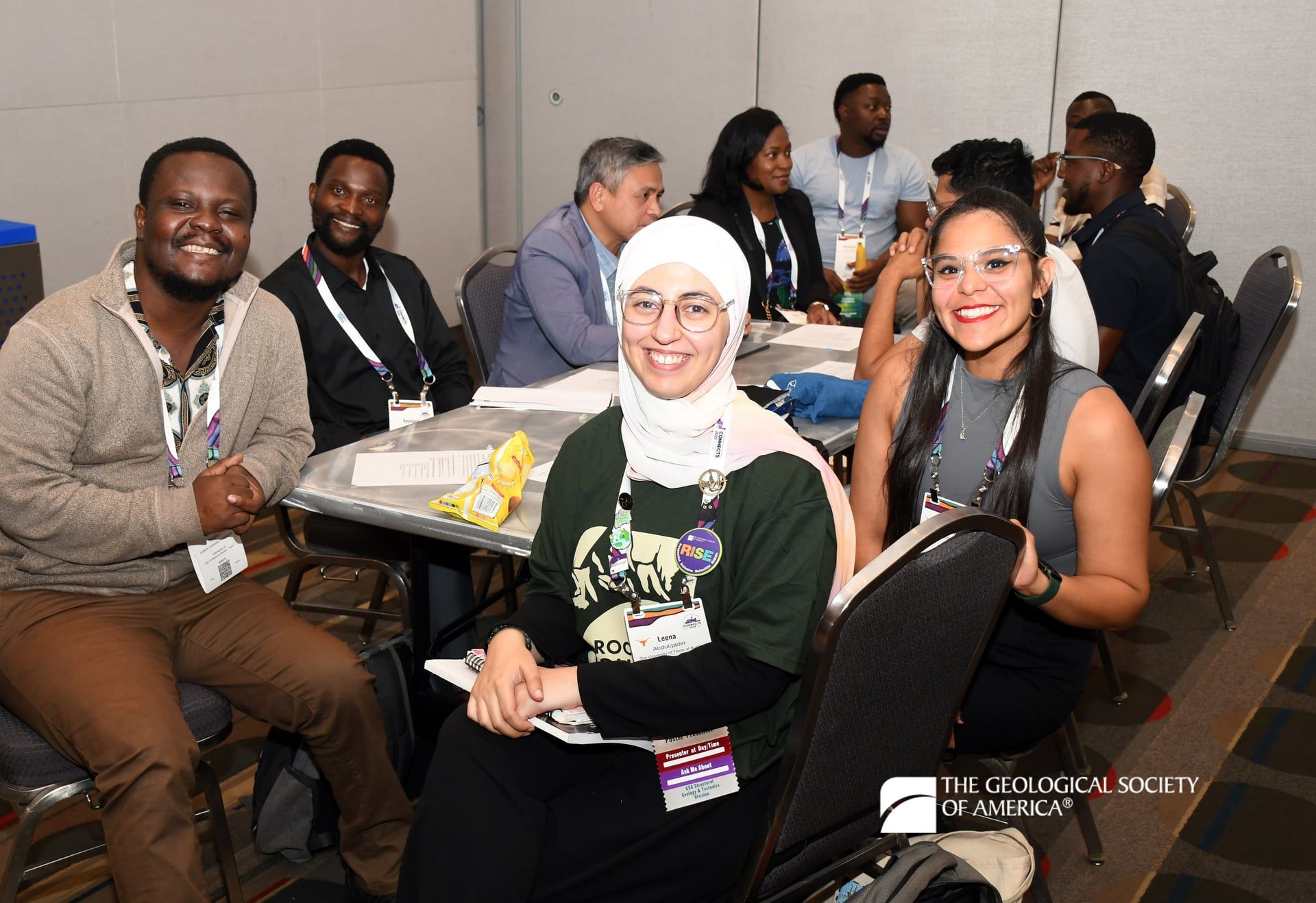 Four smiling GSA Connects 2025 attendees sit at a table and face the camera as they network at a meeting event.
