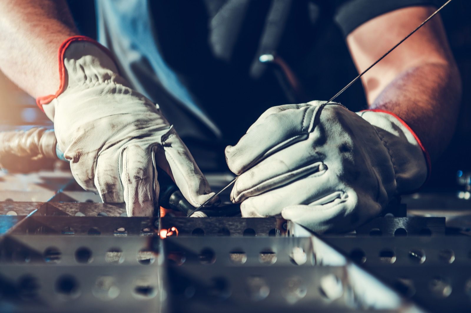A welder's gloved hands joining metal at a workbench