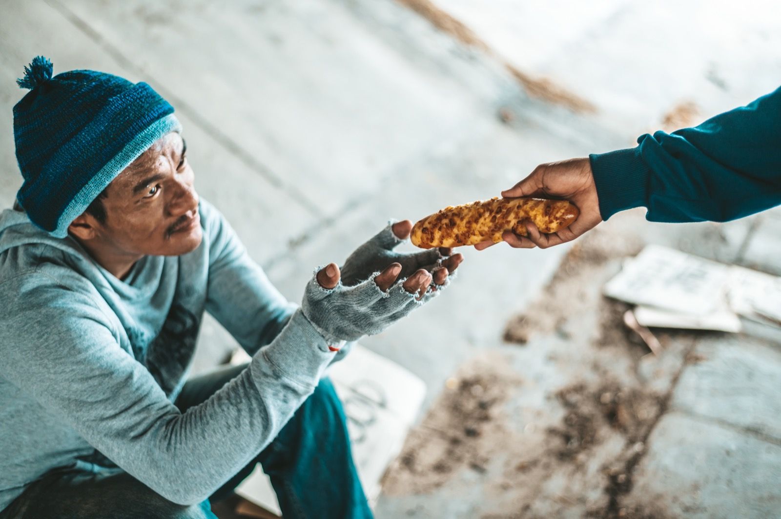 A hand offering fresh bread to a man on the street