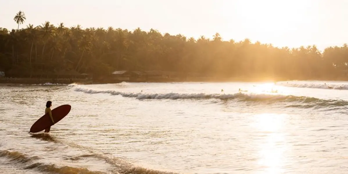 Surfer walking into the waves at sunset in Hiriketiya