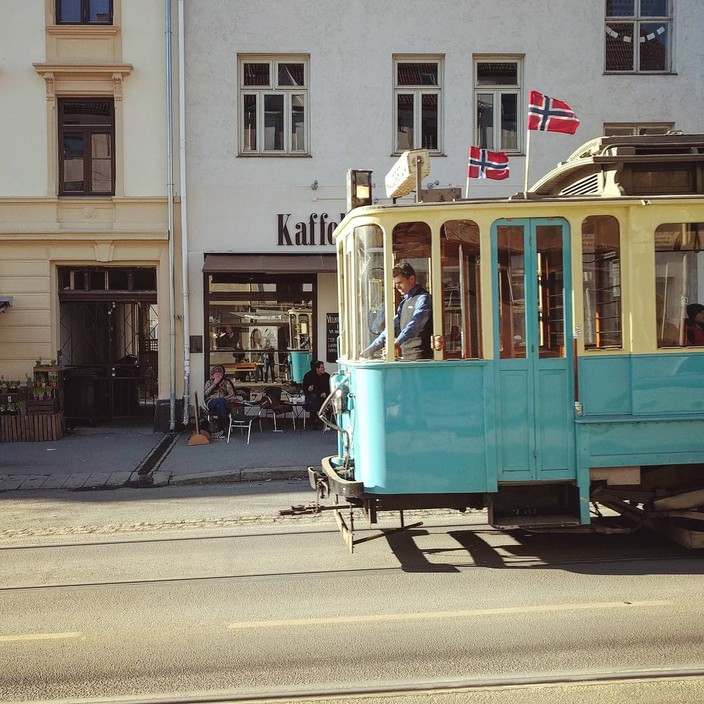 Old tram rolling down the street on a sunny day, Norwegian flags on the roof