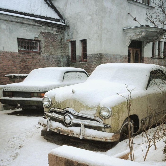 Snowed down old cars in front of a decaying building