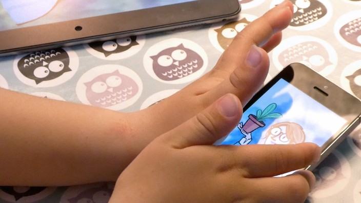 Close-up of a child’s hands holding an iPhone. The iPhone displays a storybook character.