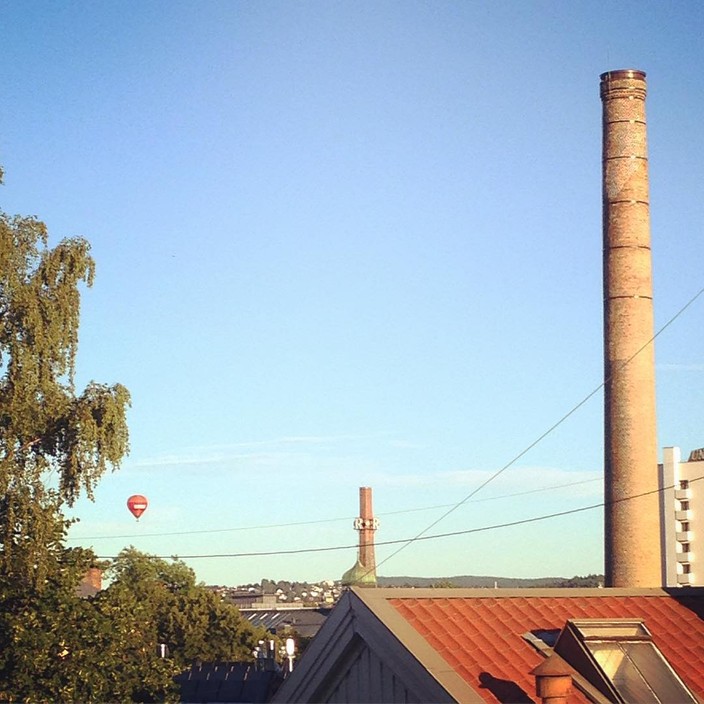 A hot air balloon floating over Oslo. Tall brick chimneys in the foreground.
