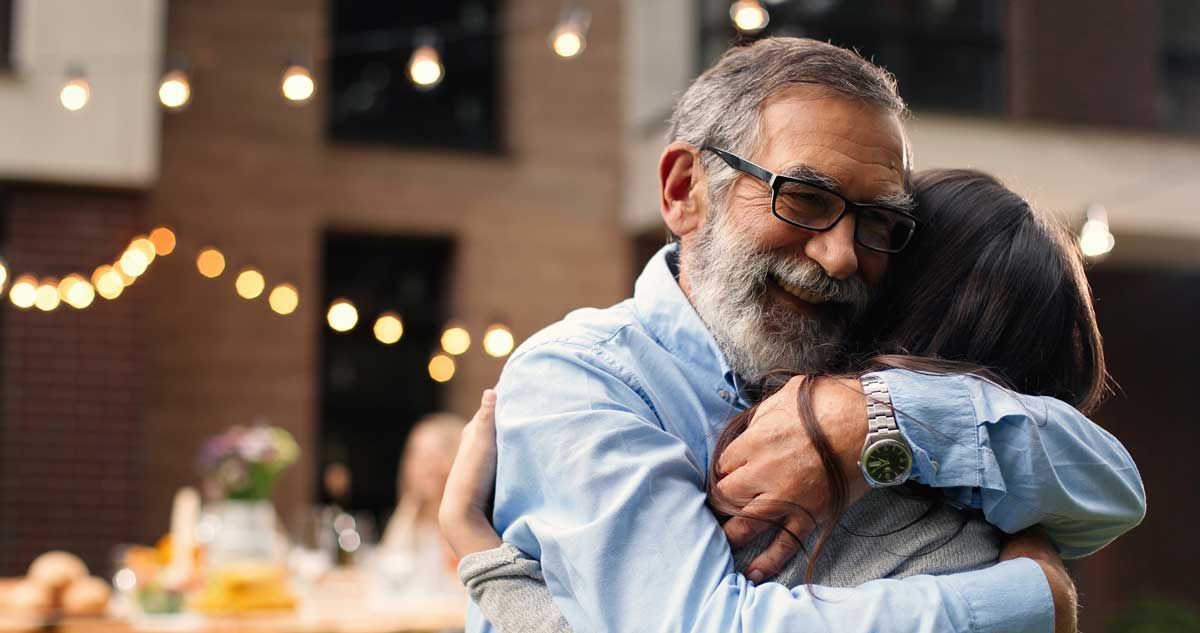 An older man in glasses hugging a woman with dark hair