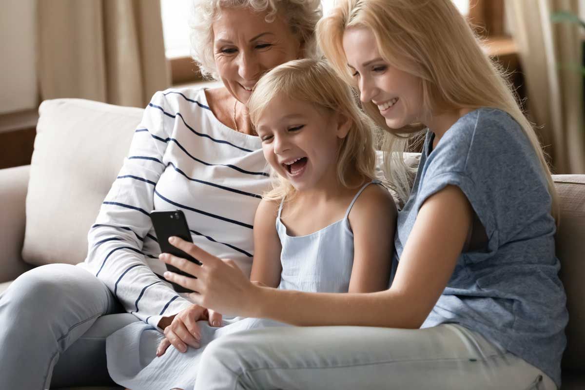 An older woman, a small girl, and a younger woman sitting next to each other smiling at a phone