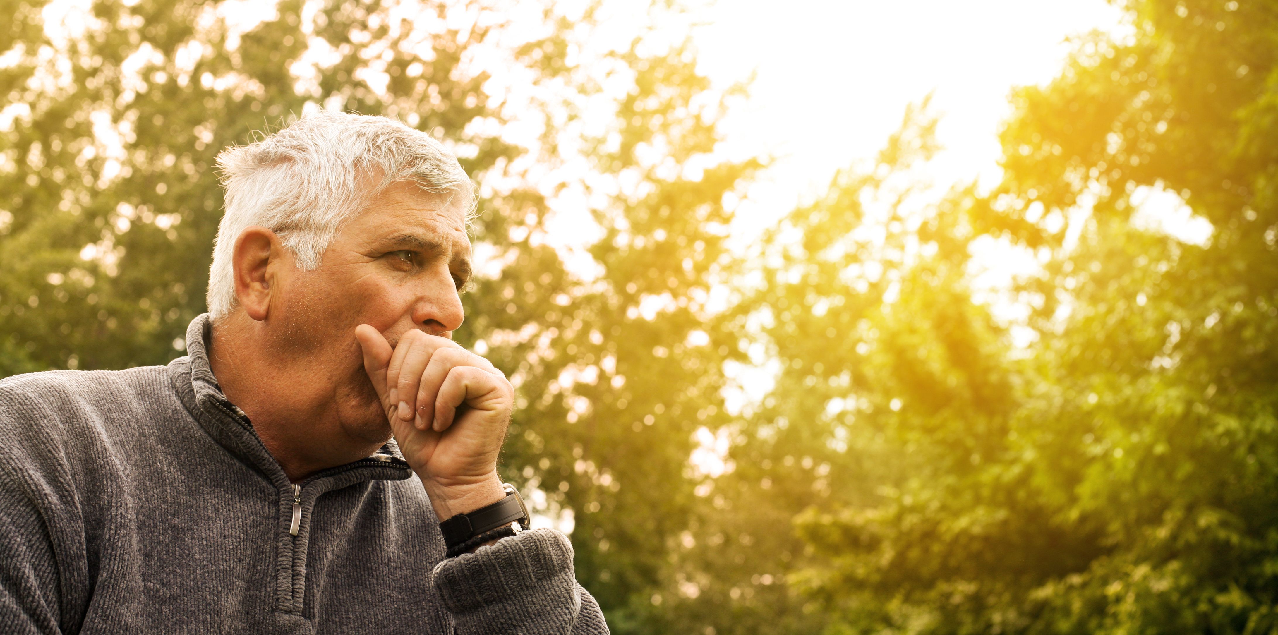 Man is coughing in front of trees that are lit up by the sun