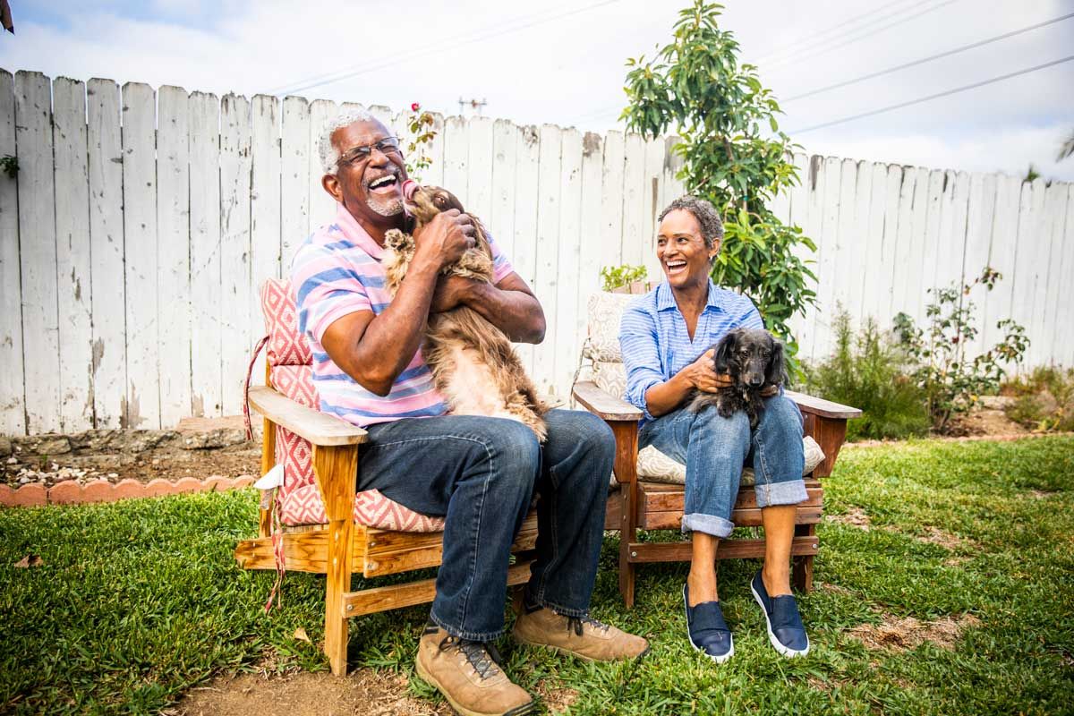 Man and woman sitting in chairs outside, happily holding dogs on their laps