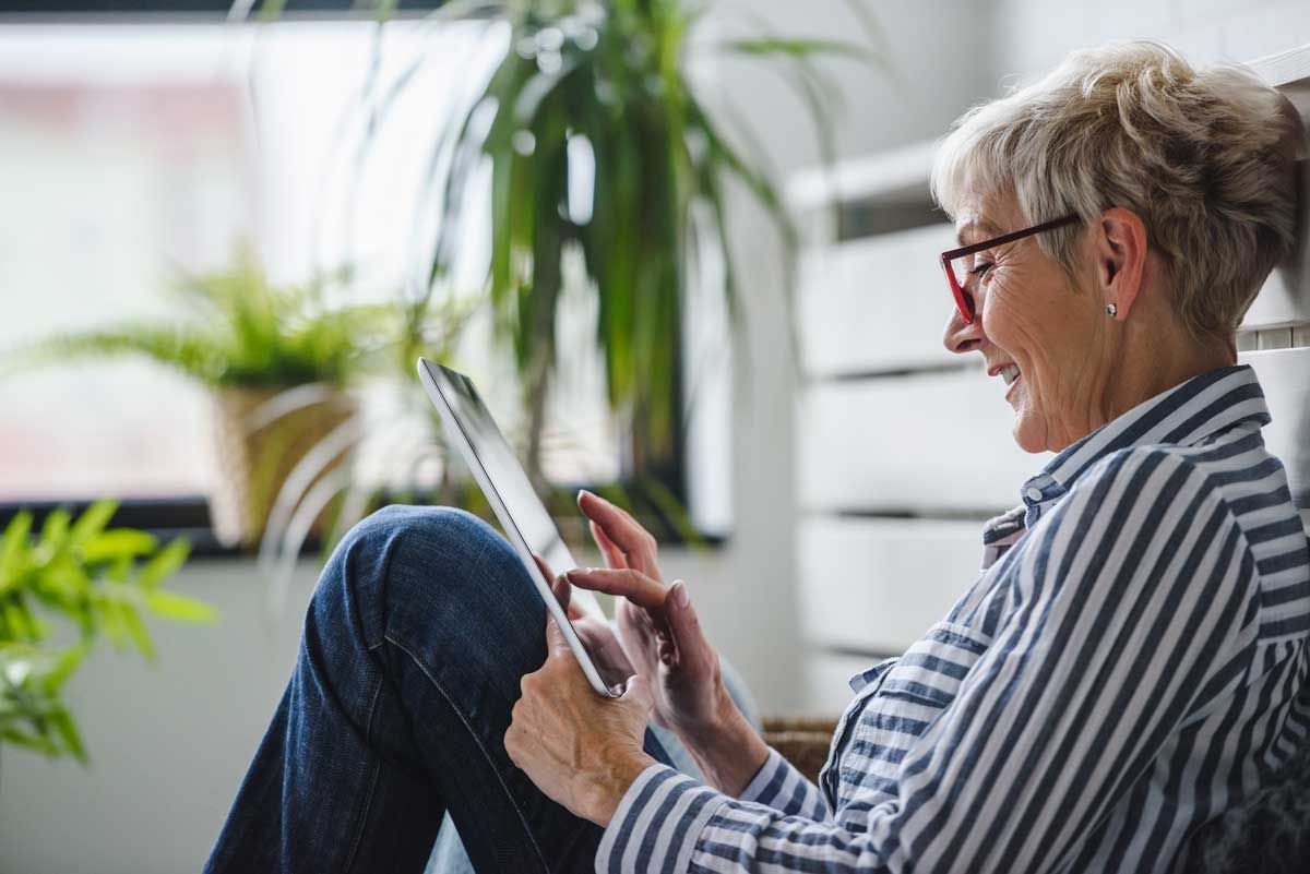 A woman in a striped shirt smiling while using her tablet computer