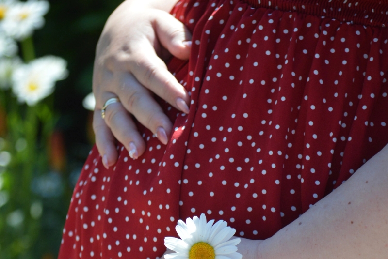 Gravid kvinde i rød kjole holder på maven