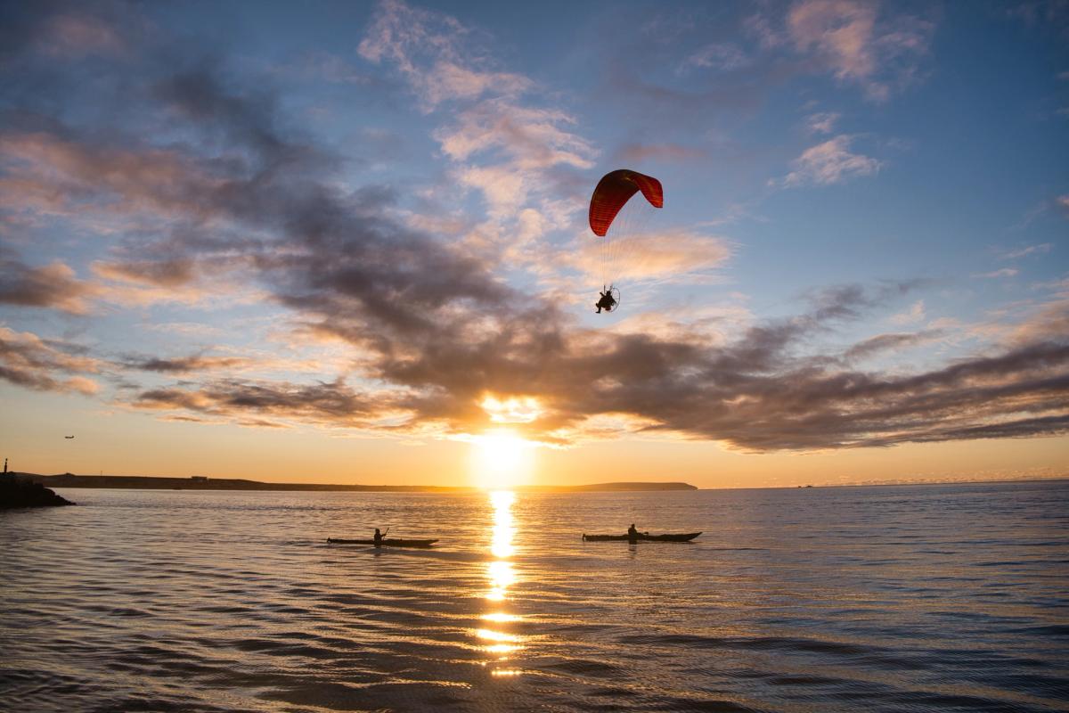 Sylvestre Campe (Film Director) flies above Nome harbour in a paramotor, with two kayakers below. Credit: Alex Rockström