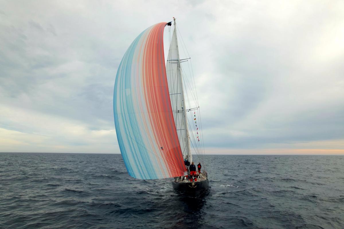 Keith Tuffley stands at the helm of the Abel Tasman, flying the climate stripes. Credit: Ramon Gonçalves, MEDIA.etc