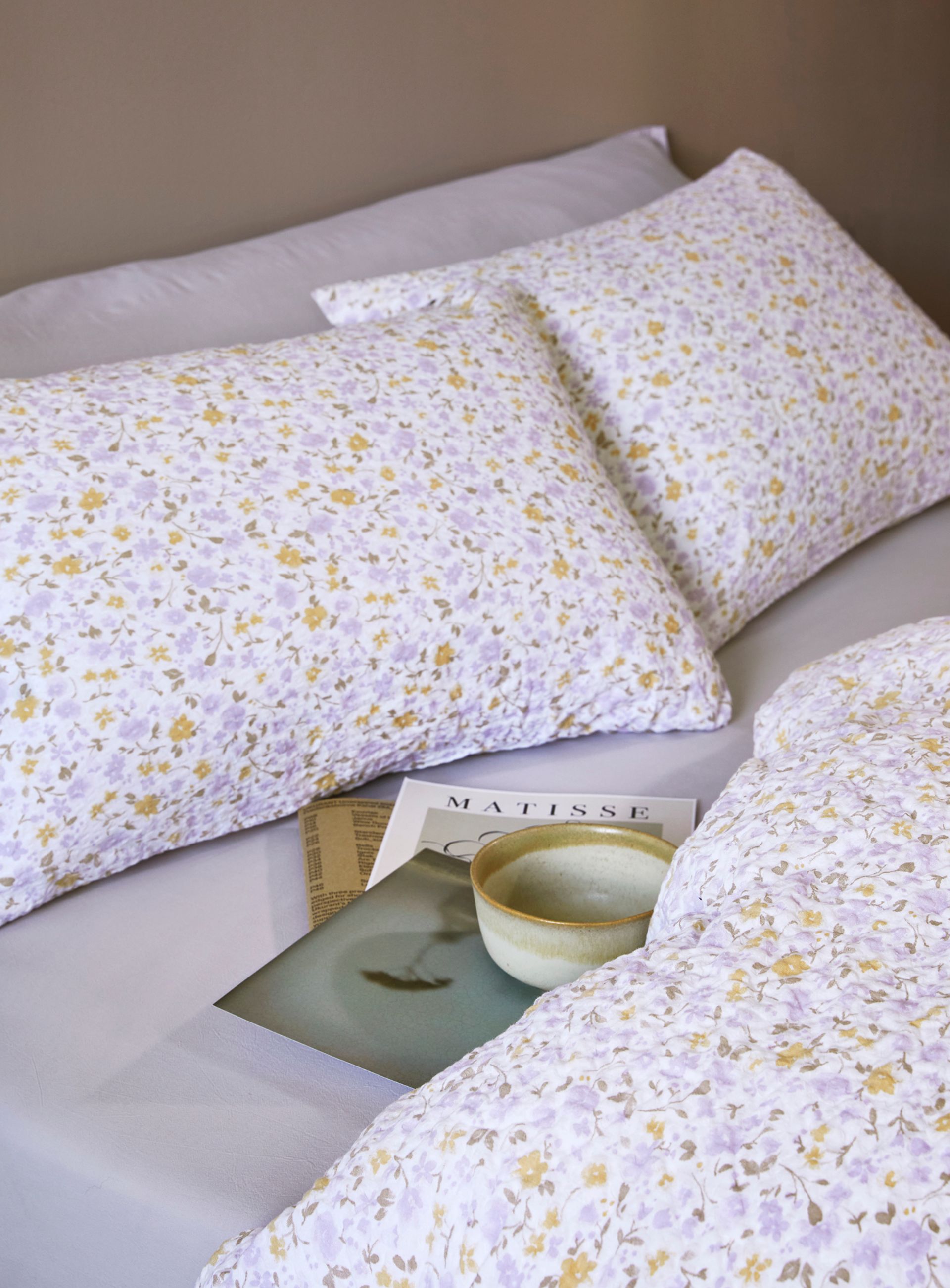 Oppredd seng med Høie Tor og Frøya sengesett i lyseblå nyanser – en kombinasjon av ensfarget og stripete bomullssateng, som gir et mykt og harmonisk uttrykk i et lyst soverom med naturlig dagslys.