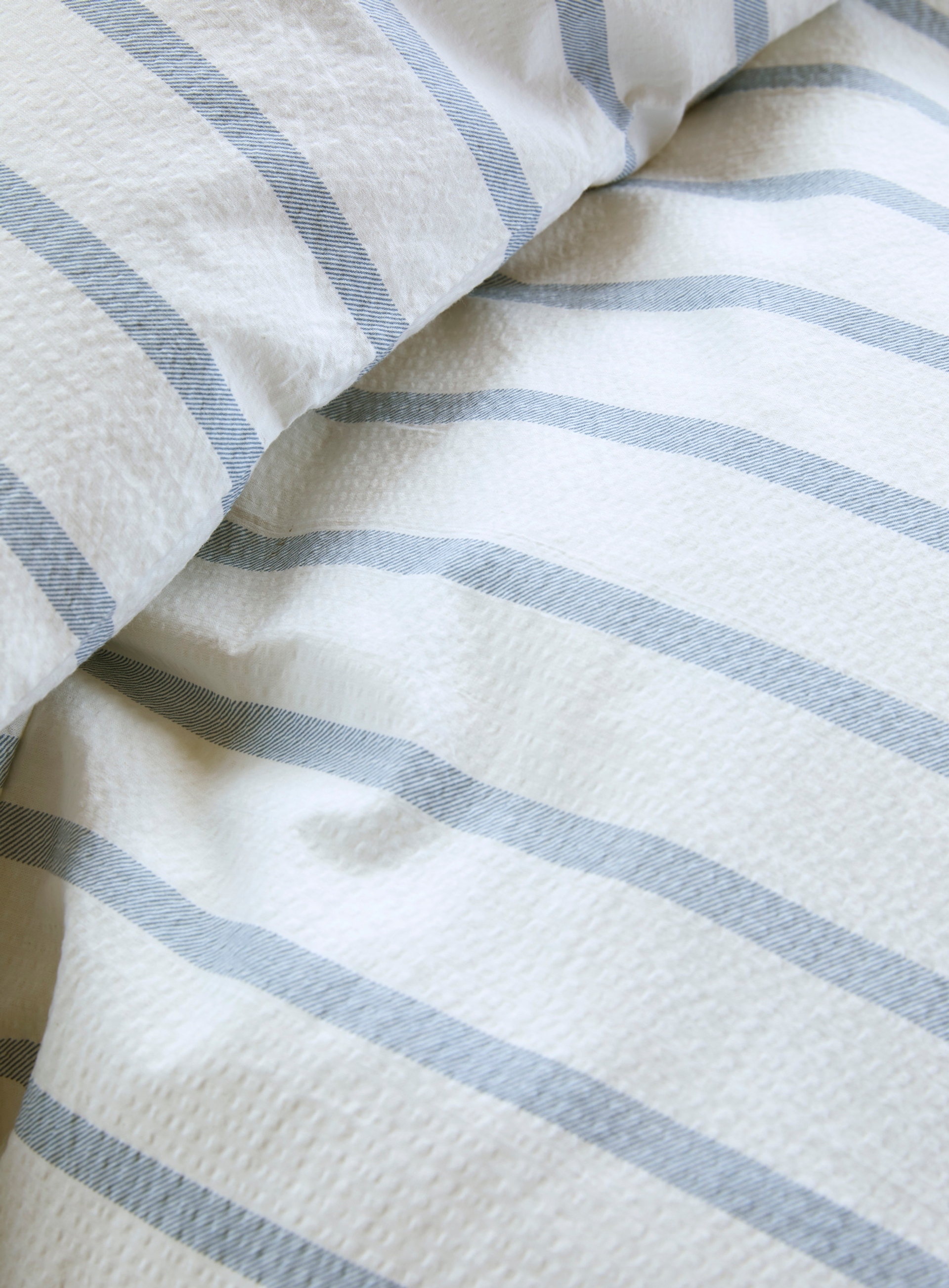 Nærbilde av Høie Eilert sengesett i blå og hvit stripet krepp – vevd struktur som gir en luftig, bølget overflate og et avslappet uttrykk.