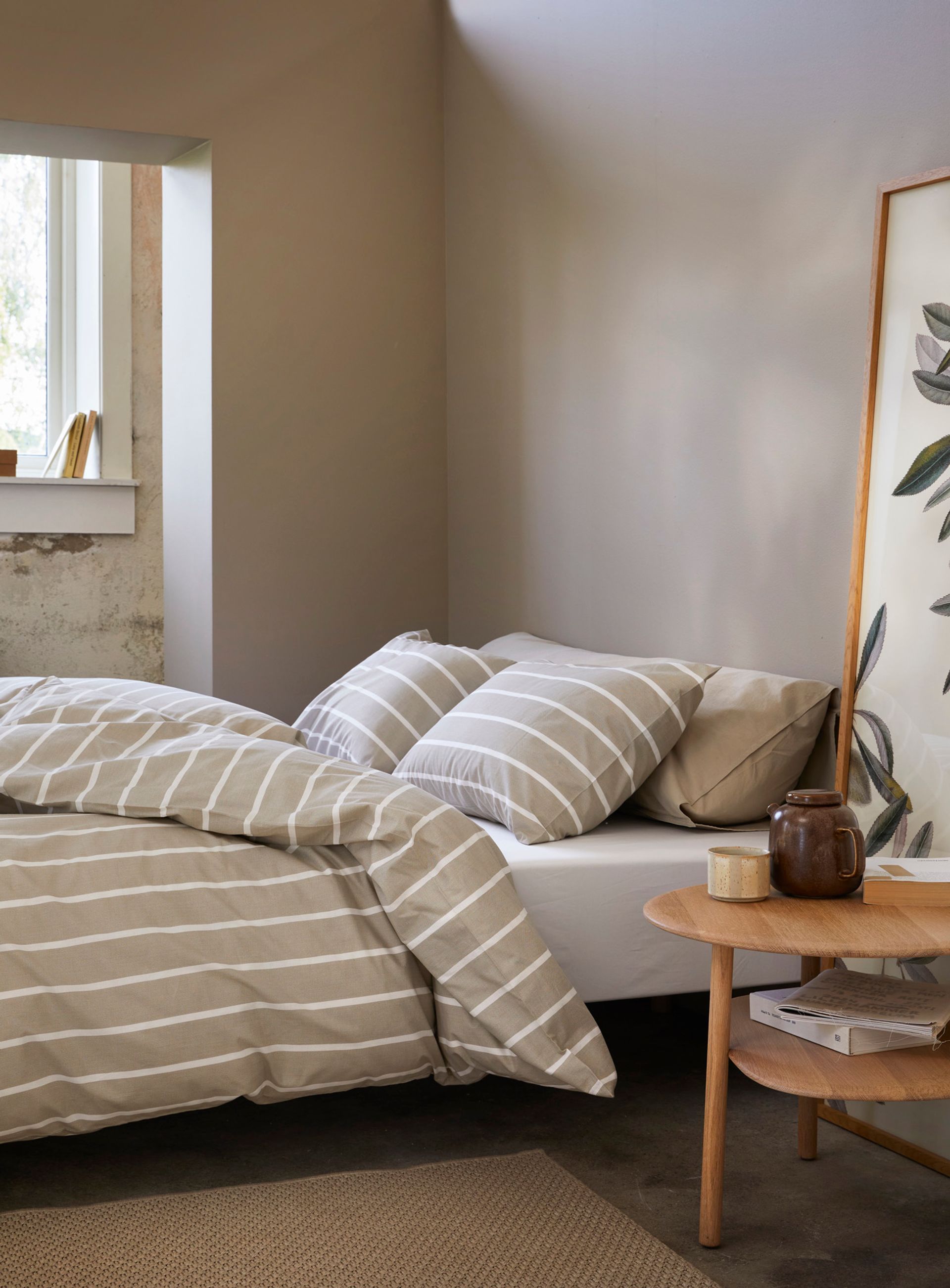 Nærbilde av oppredd seng med Høie Tor og Frøya sengesett i beige – en avslappet miks av smale striper og ensfarget bomull, som skaper en rolig og lun atmosfære på soverommet.