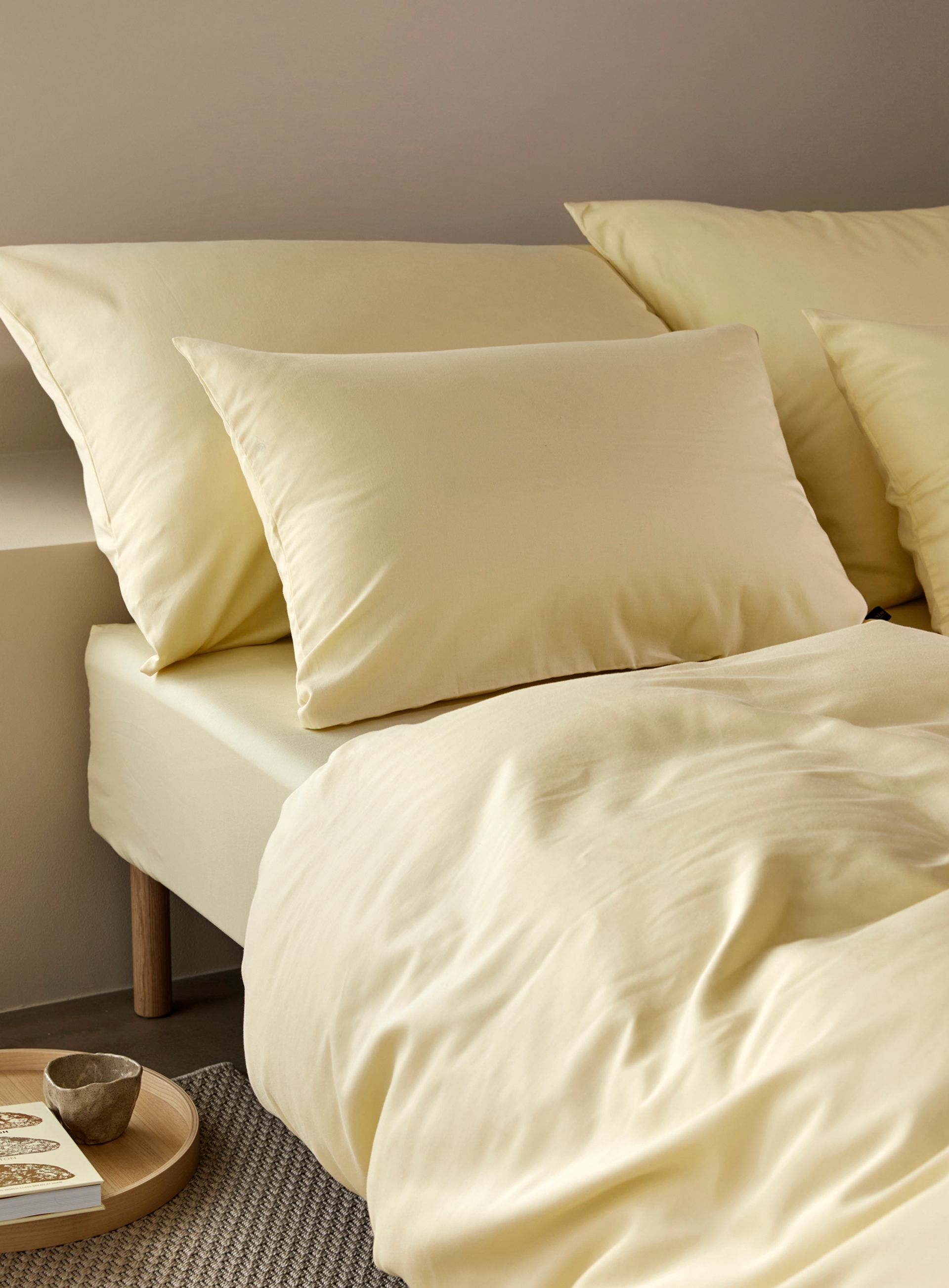 Nærbilde av oppredd seng med Høie Tor og Frøya sengesett i beige – en avslappet miks av smale striper og ensfarget bomull, som skaper en rolig og lun atmosfære på soverommet.