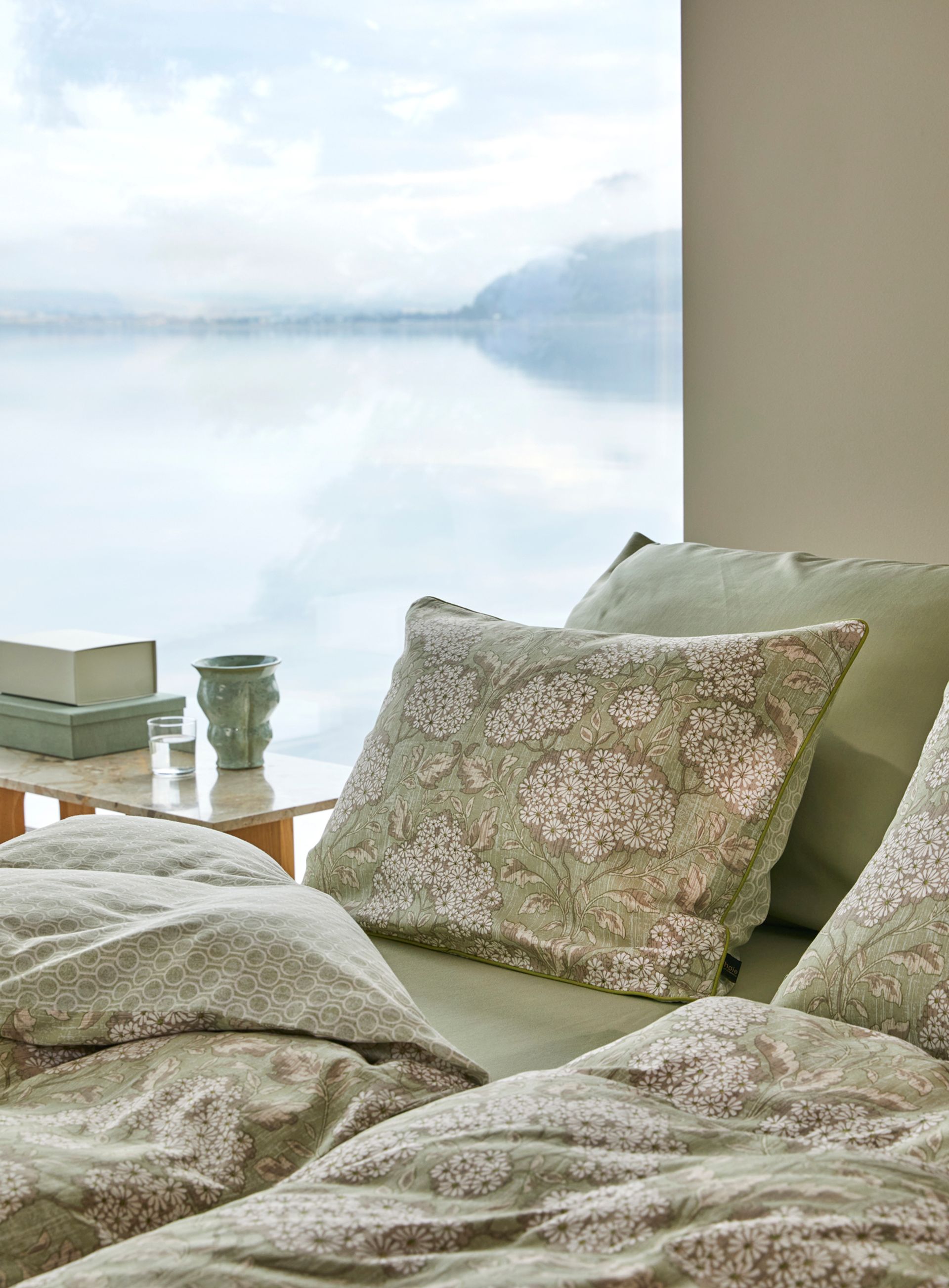 Nærbilde av oppredd seng med Høie Tor og Frøya sengesett i beige – en avslappet miks av smale striper og ensfarget bomull, som skaper en rolig og lun atmosfære på soverommet.