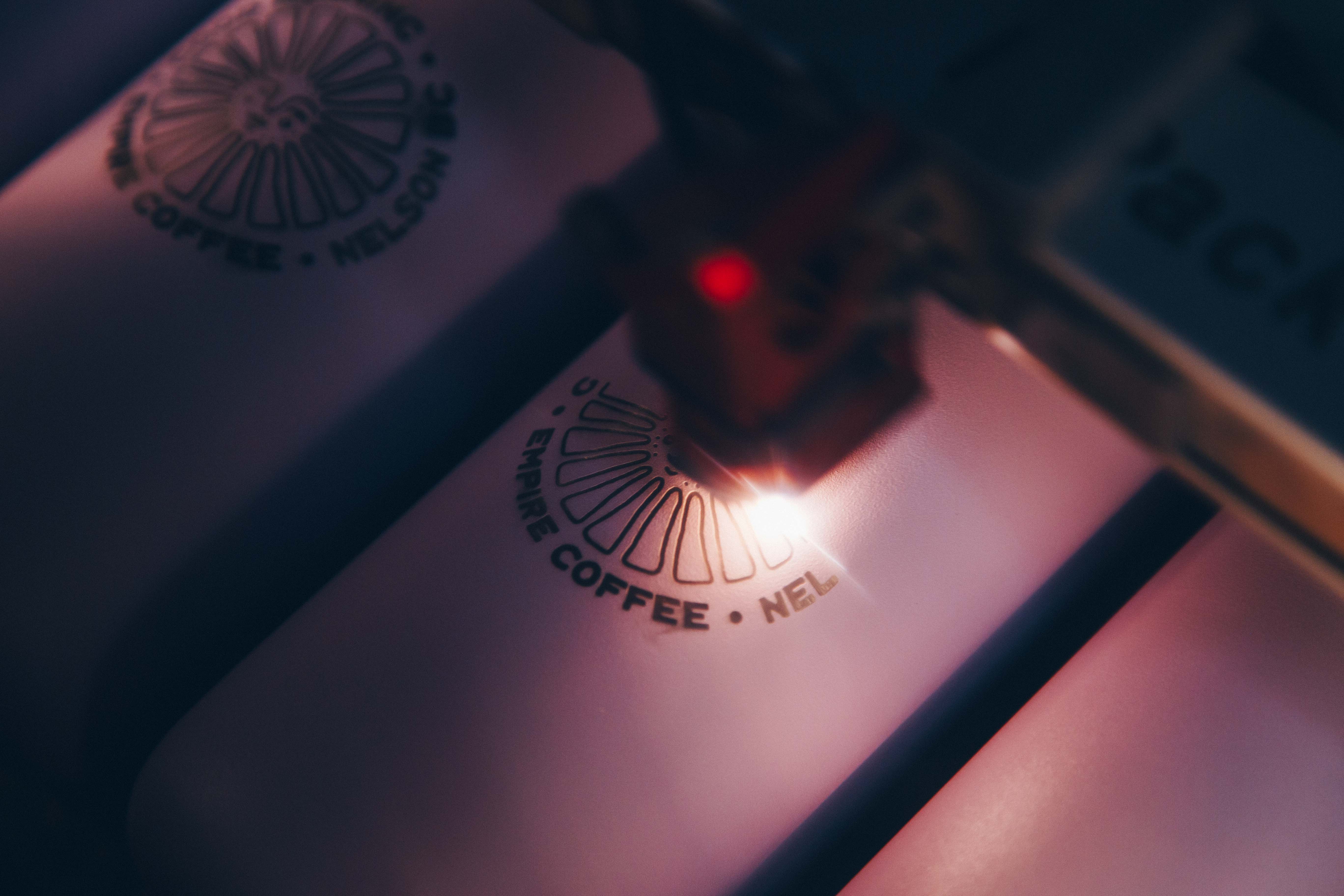 Laser engraver machine engraving a logo into a travel coffee cup.