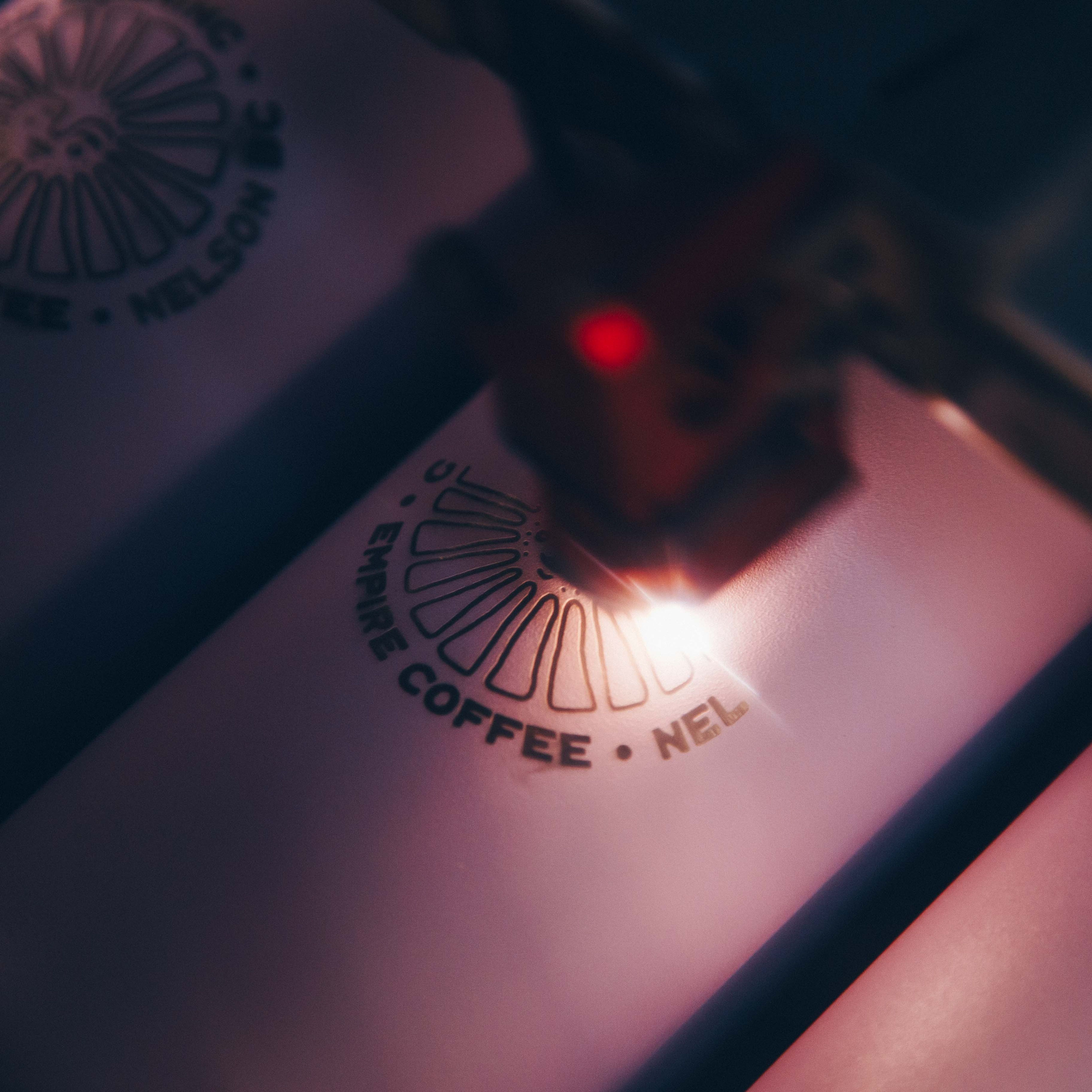 Laser engraver machine engraving a logo into a travel coffee cup.