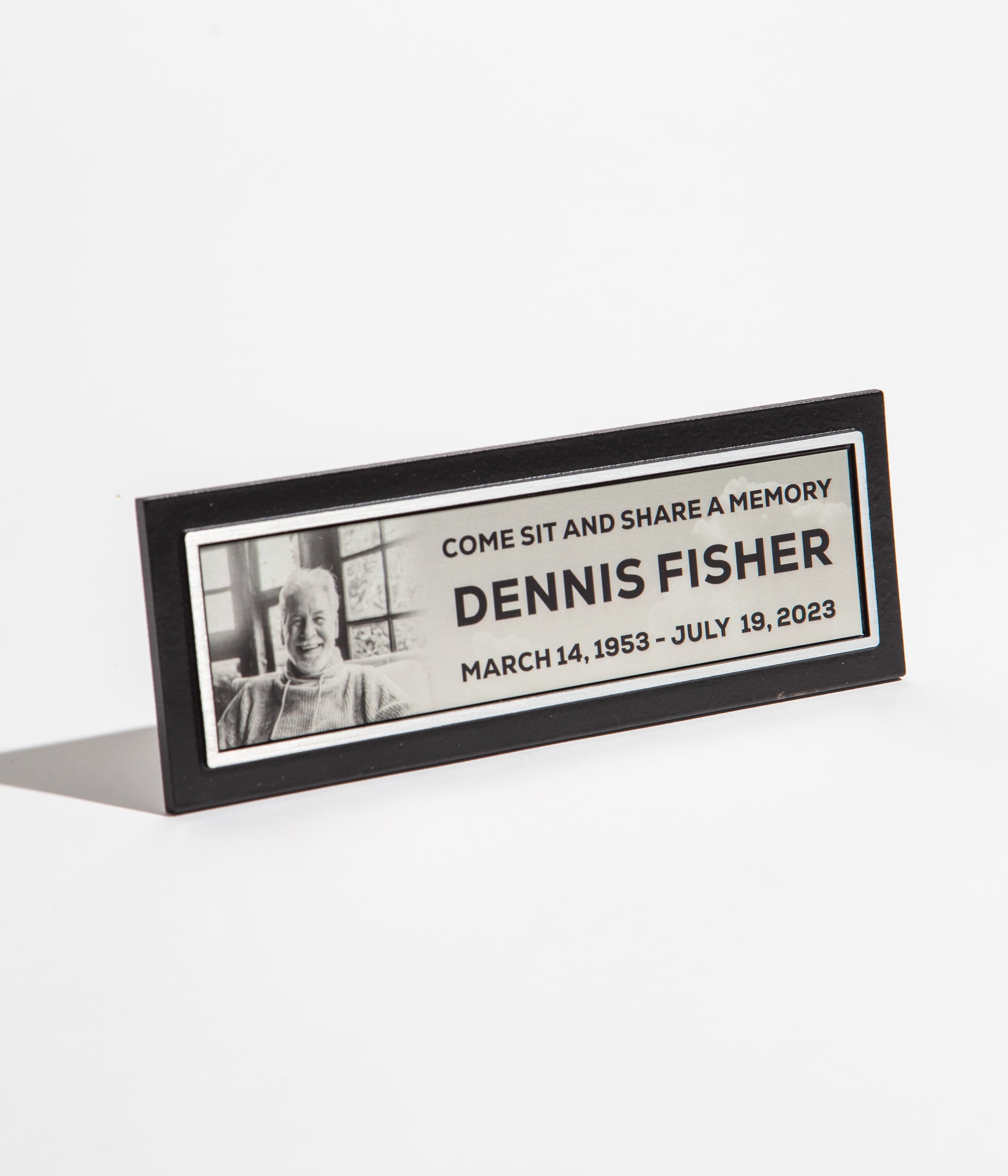 Memorial plaque with a photo and text commemorating Dennis Fisher, dated March 14, 1953 - July 19, 2023.