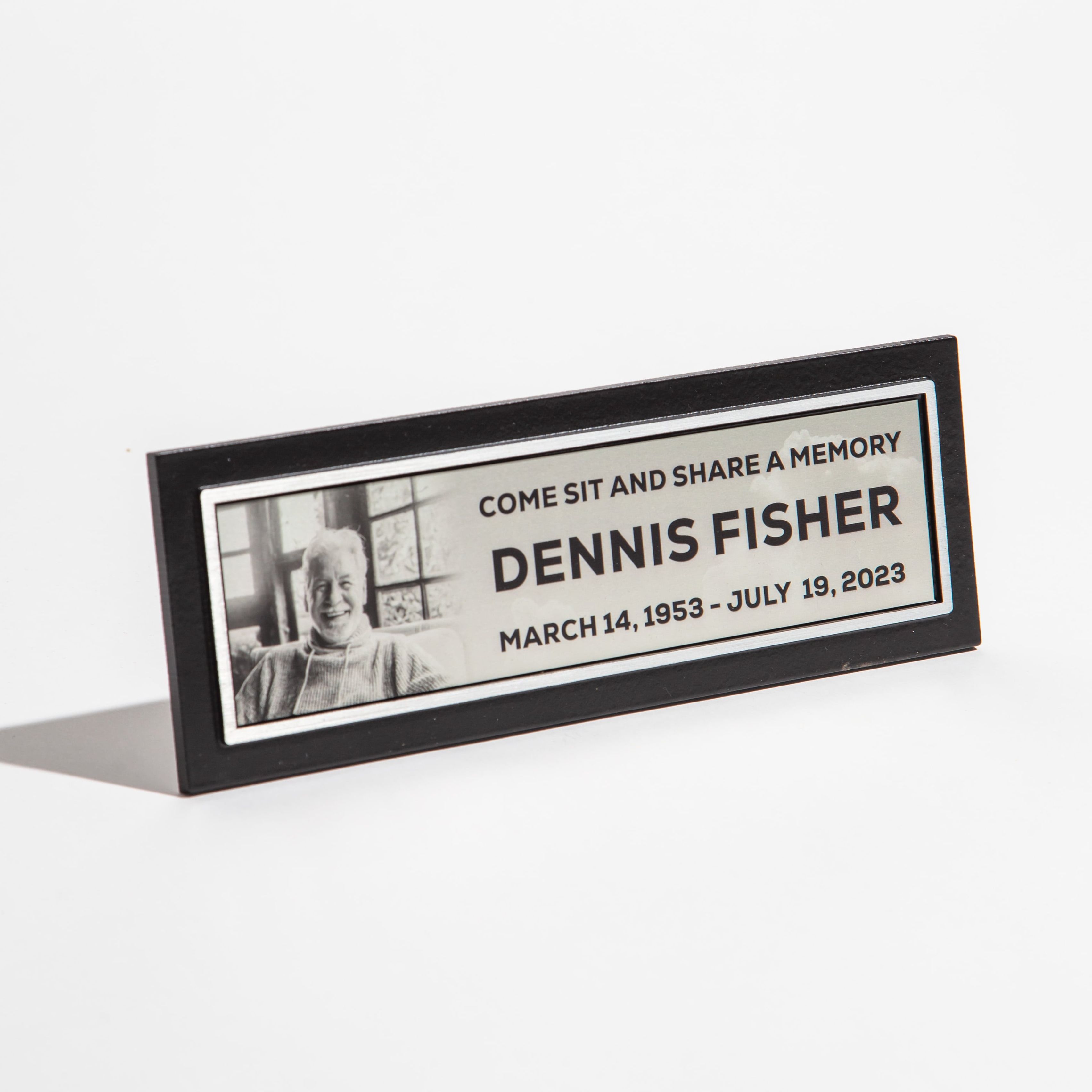 Memorial plaque with a photo and text commemorating Dennis Fisher, dated March 14, 1953 - July 19, 2023.